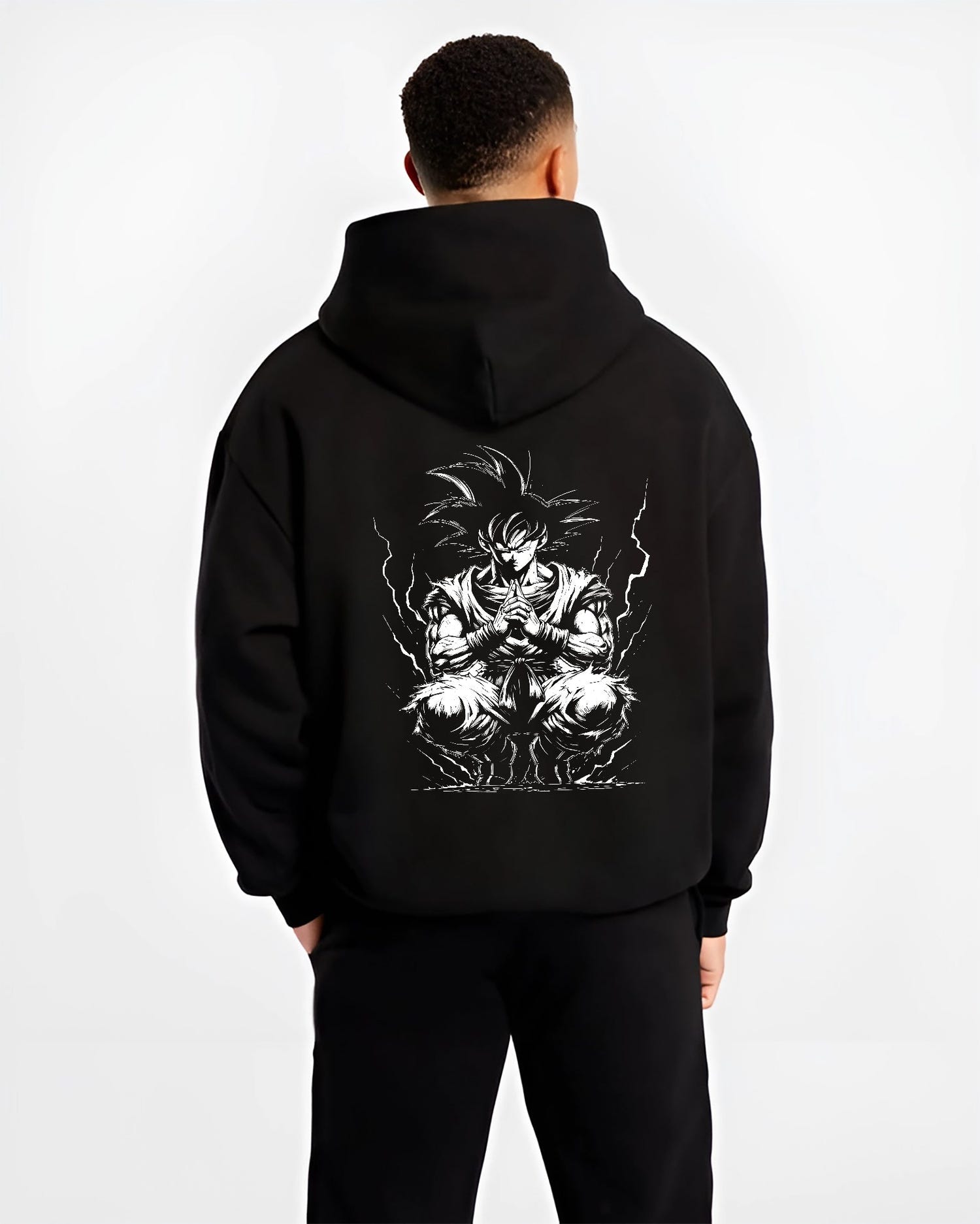 Black hoodie worn by a male model, back view, featuring Dragon Ball Goku retro manga graphic in meditation pose with glowing aura in anime poster inspired style.