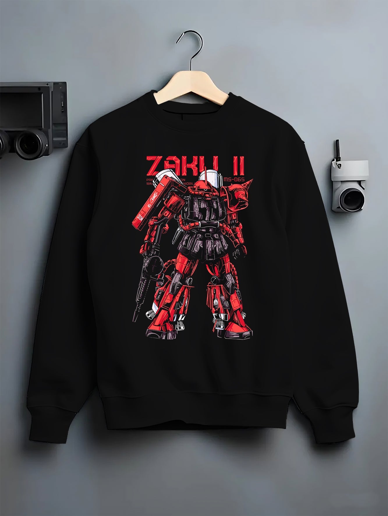 Black crewneck sweatshirt on a hanger against a grey wall, featuring Zaku II retro mecha Gundam inspired design in anime poster style artwork.