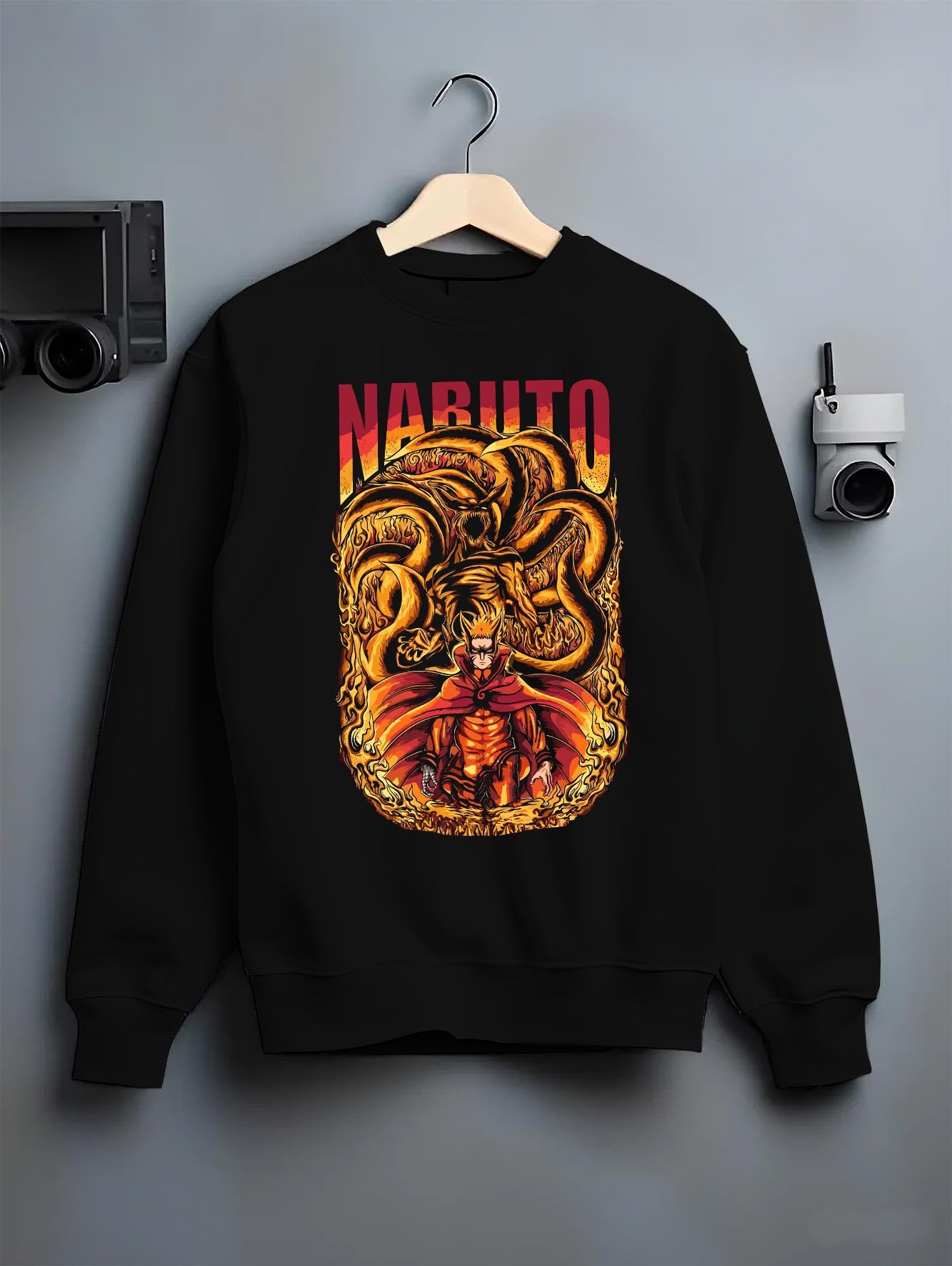 Black crewneck sweatshirt on a hanger against a grey wall, featuring Naruto Kurama fiery shonen battle retro manga poster style artwork.
