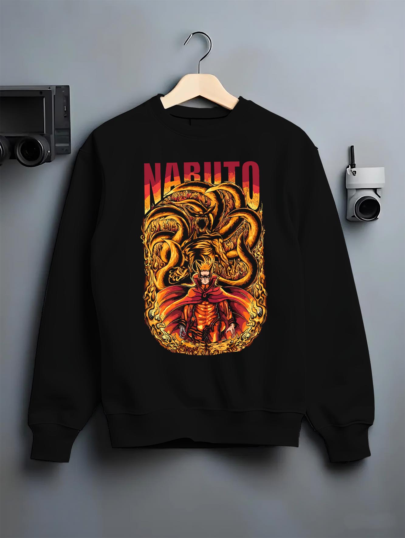 Black crewneck sweatshirt on a hanger against a grey wall, featuring Naruto Kurama fiery shonen battle retro manga poster style artwork.
