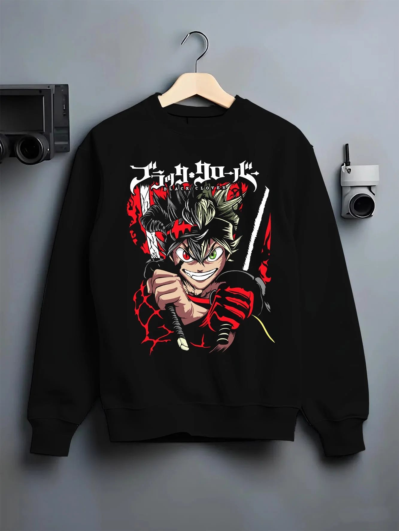 Black crewneck sweatshirt on hanger with Asta Battle Hoodie Black Clover Fierce Grin Warrior graphic premium wear.