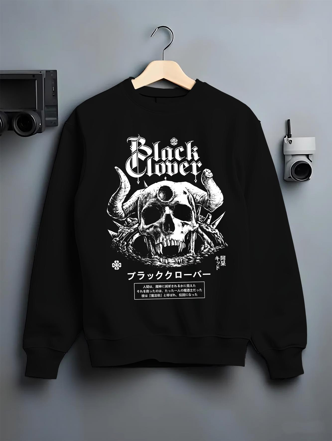Black crewneck sweatshirt on a hanger against a grey wall, featuring Black Clover skull retro manga panel artwork with Japanese animation streetwear design.