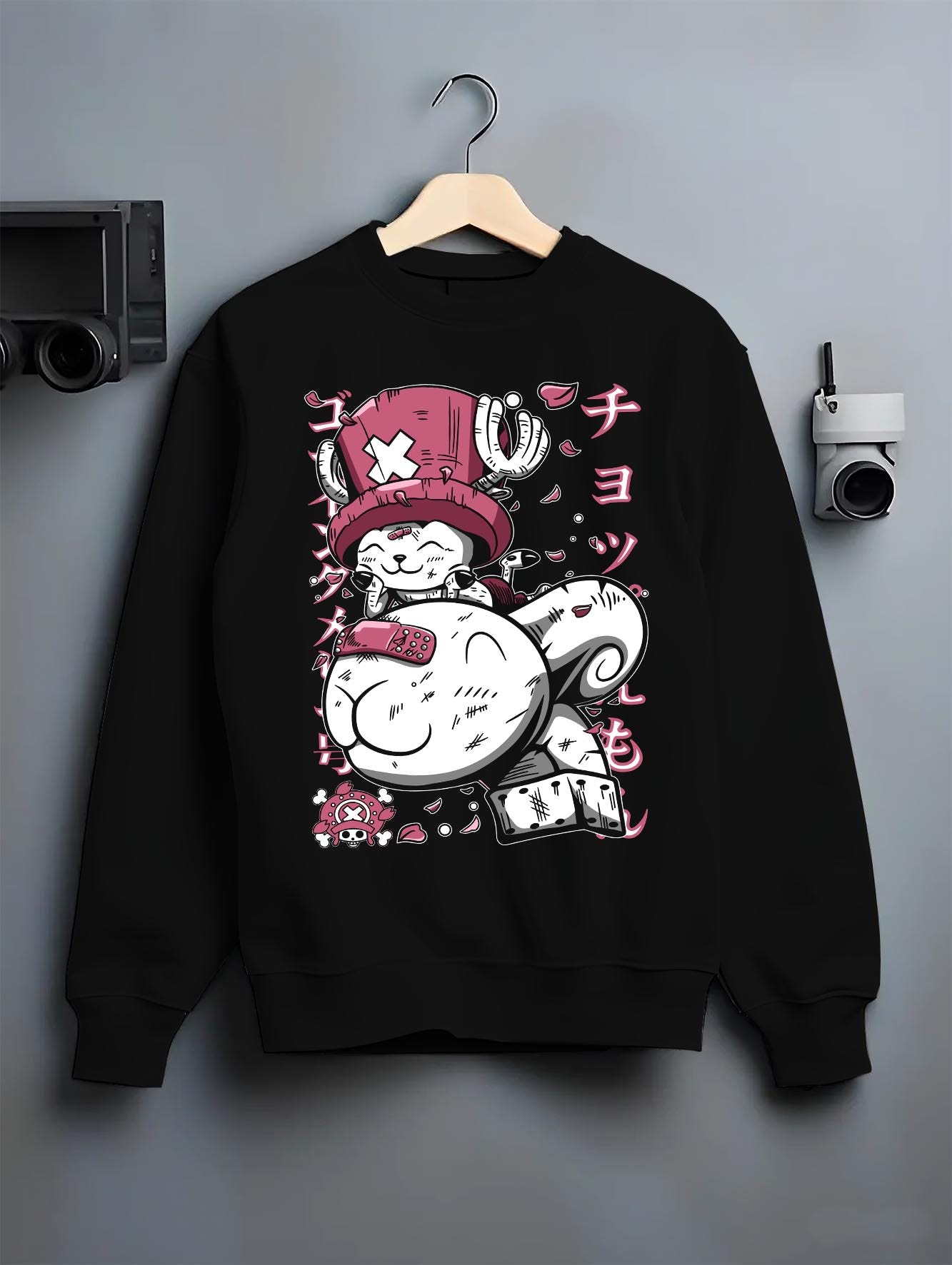 Black crewneck sweatshirt on a hanger against a grey wall, featuring Tony Tony Chopper Japanese animation streetwear style design in bold pink manga aesthetic.