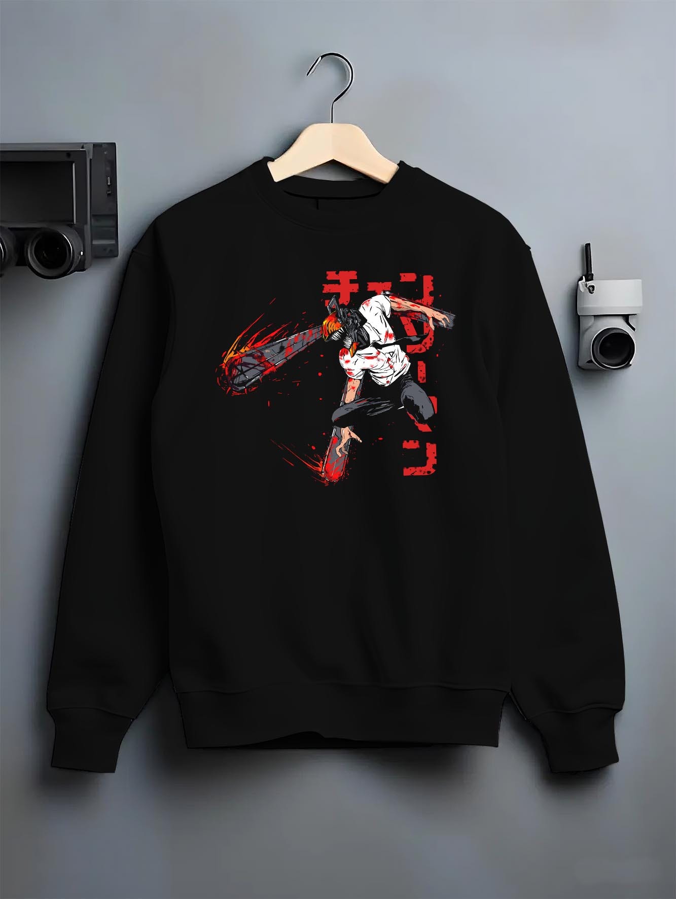 Black crewneck sweatshirt on a hanger against a grey wall, featuring Chainsaw Man Denji dark manga panel artwork in retro streetwear graphic style inspired by Japanese animation.