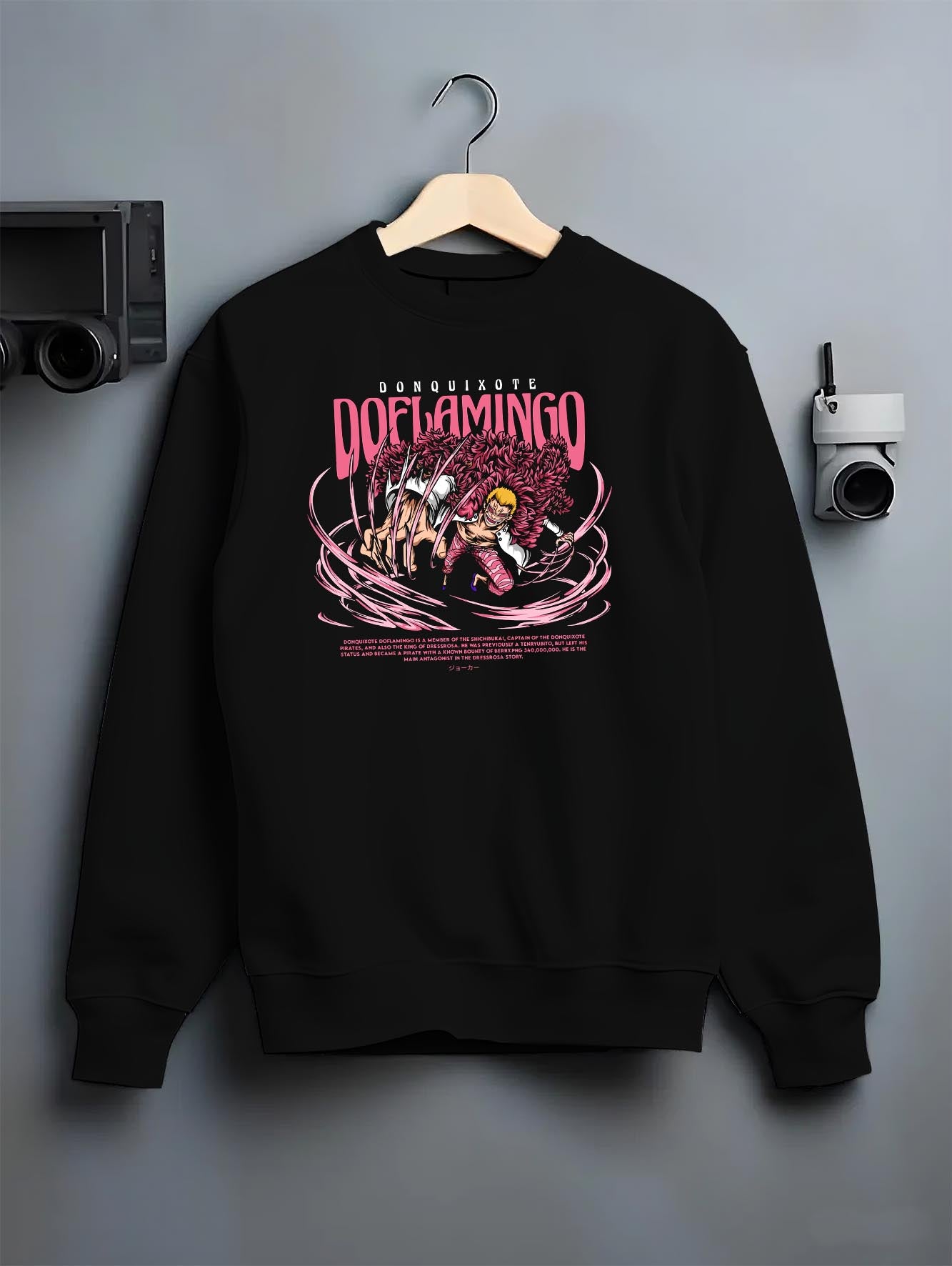 Black crewneck sweatshirt on a hanger against a grey wall, featuring One Piece Doflamingo anime poster inspired artwork with string powers in bold retro manga style.