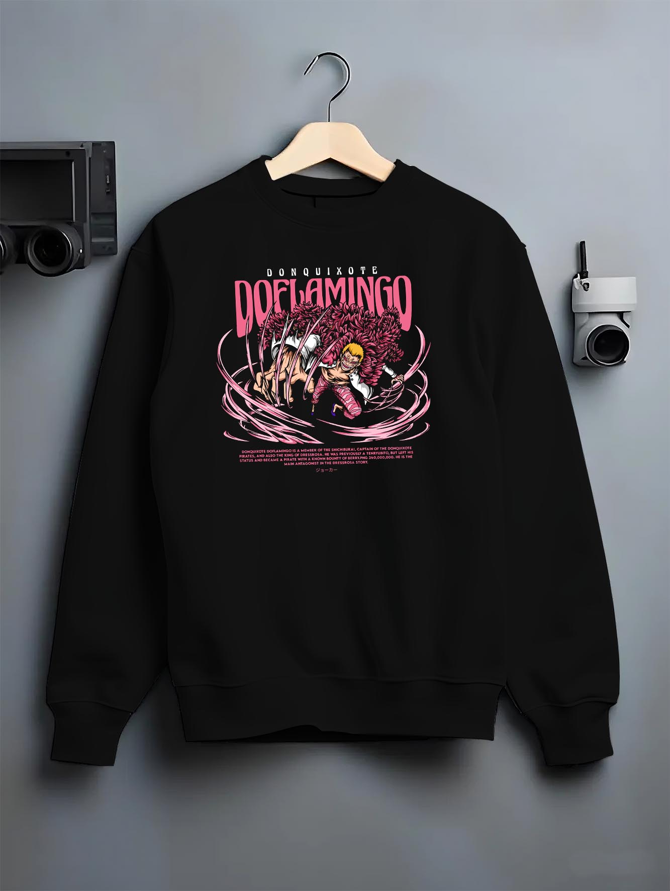 Black crewneck sweatshirt on a hanger against a grey wall, featuring One Piece Doflamingo anime poster inspired artwork with string powers in bold retro manga style.