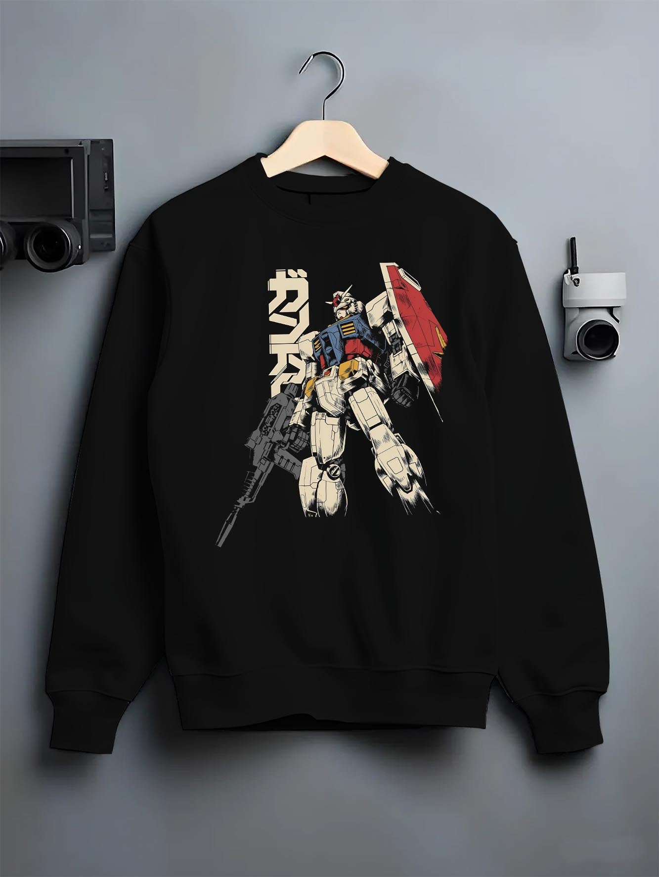 Black crewneck sweatshirt on a hanger against a grey wall, featuring Mobile Suit Gundam retro manga panel inspired design with detailed giant mecha anime artwork.