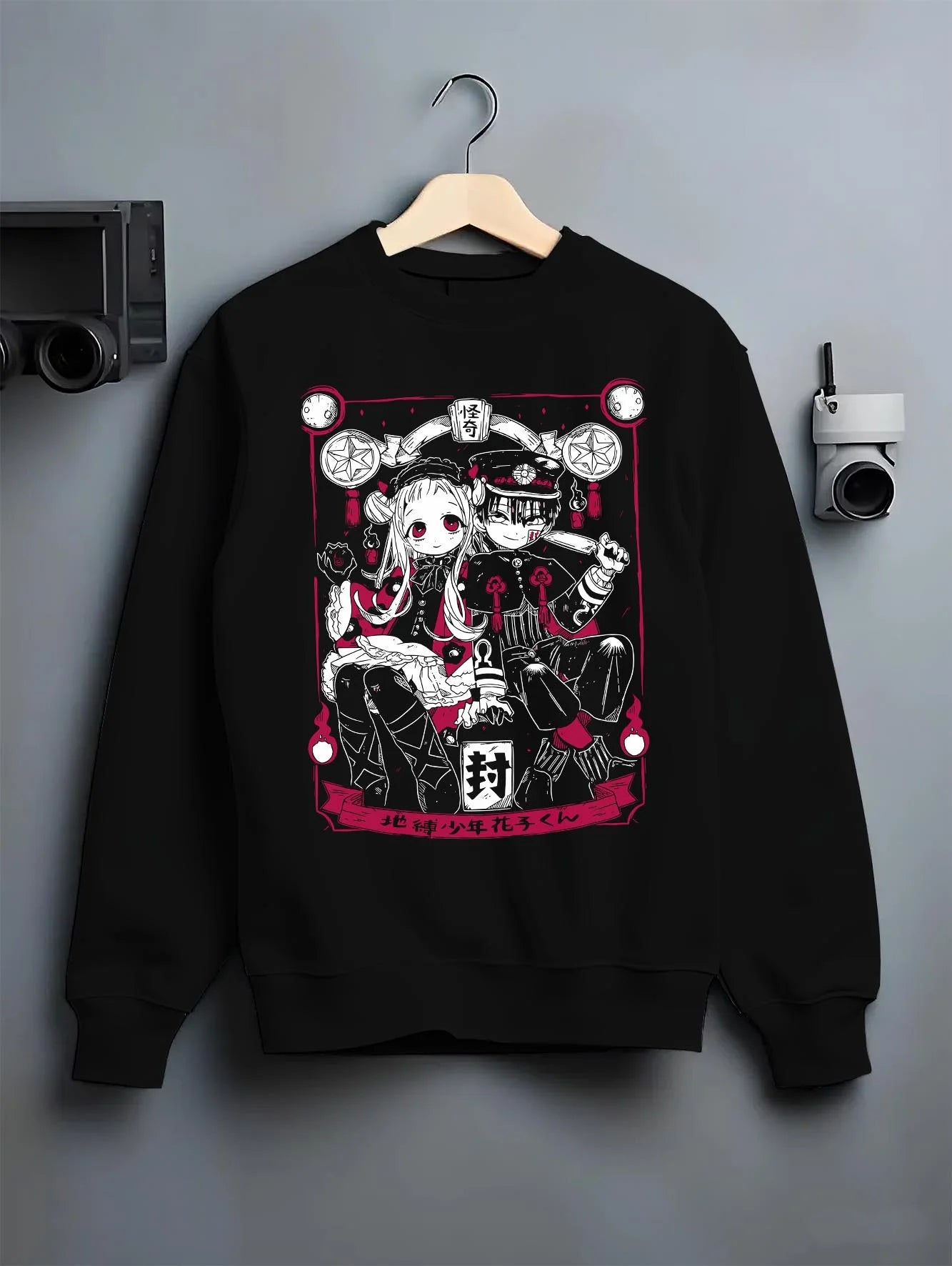 Black crewneck sweatshirt on hanger against grey wall, featuring cult classic anime poster inspired Hanako-kun and Nene Yashiro retro streetwear graphic.