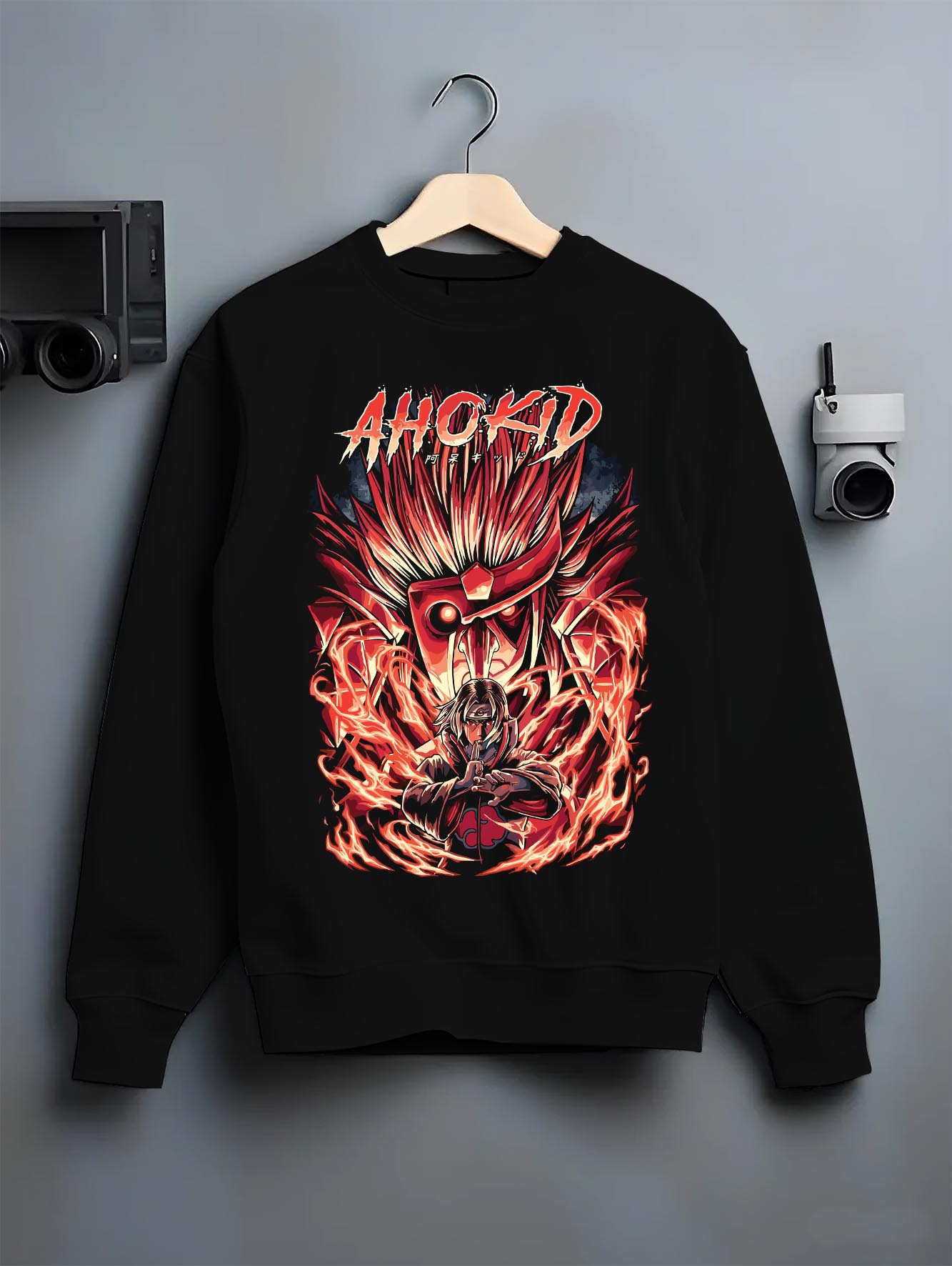 Black crewneck sweatshirt on a hanger against a grey wall, featuring Naruto Itachi Uchiha modern streetwear graphic with red Susanoo energy.