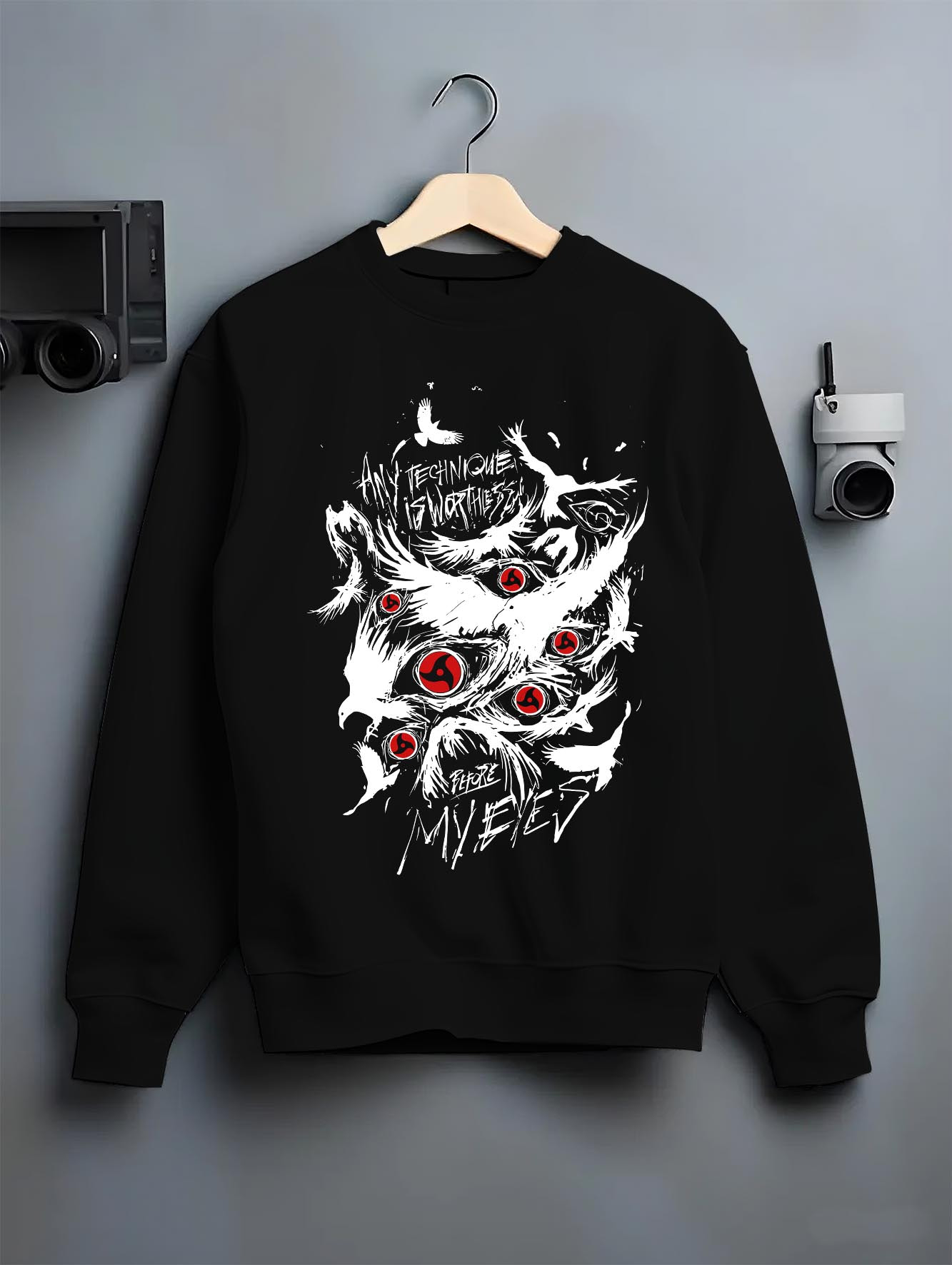 Black crewneck sweatshirt on a hanger against a grey wall, featuring Naruto Sharingan retro manga inspired graphic with distressed eye design and bold lettering.