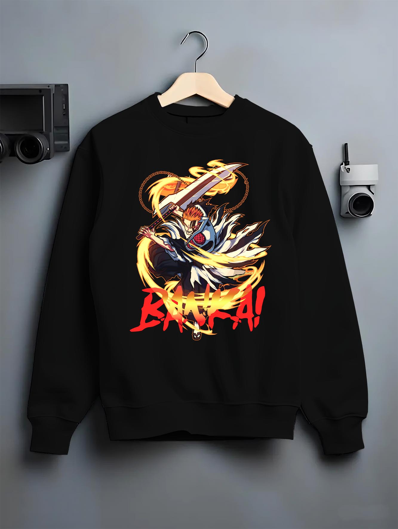 Black crewneck sweatshirt on a hanger against a grey wall, featuring Bleach Ichigo Bankai retro manga inspired battle design with striking flame aura.