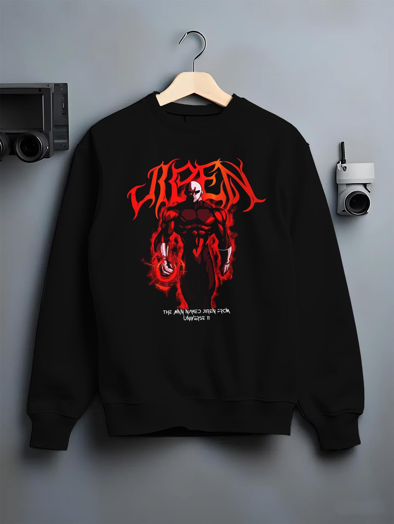 Black crewneck sweatshirt on a hanger against a grey wall, featuring Dragon Ball Super Jiren dark manga panel graphic with fiery aura and bold retro streetwear style.