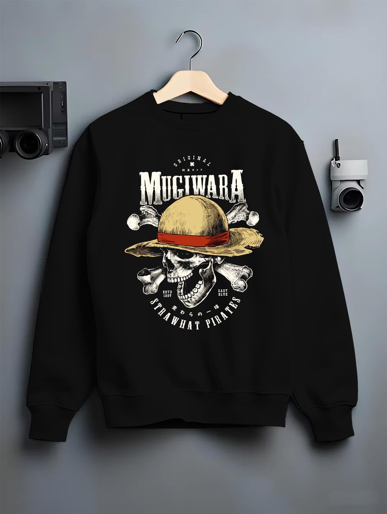 Black crewneck sweatshirt on a hanger against a grey wall, featuring One Piece Mugiwara Straw Hat Pirates skull design in anime poster inspired retro streetwear style.