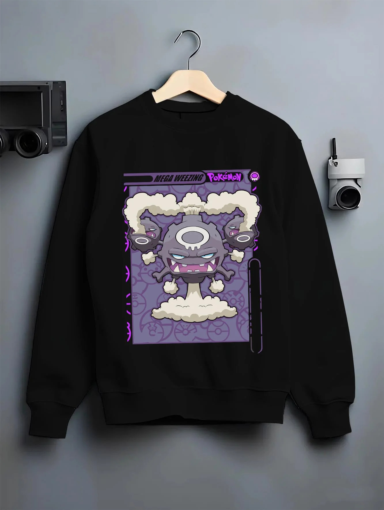 Black crewneck sweatshirt on hanger with Weezing Hoodie Pokémon Mega Evolution Card graphic premium wear.