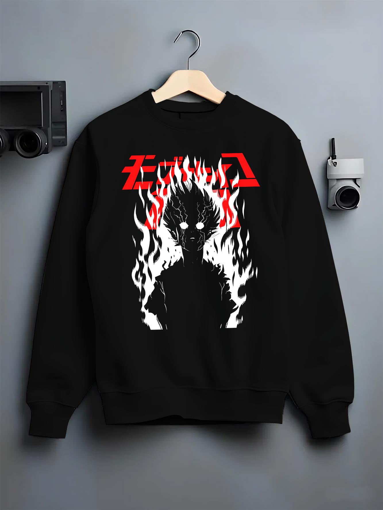 Black crewneck sweatshirt on a hanger against a grey wall, featuring Mob Psycho 100 silhouette engulfed in flames retro manga inspired artwork.