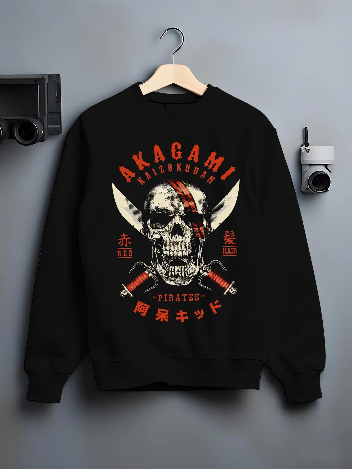 Black crewneck sweatshirt on a hanger against a grey wall, featuring Akagami Red Hair Pirates skull cult classic retro manga inspired artwork.