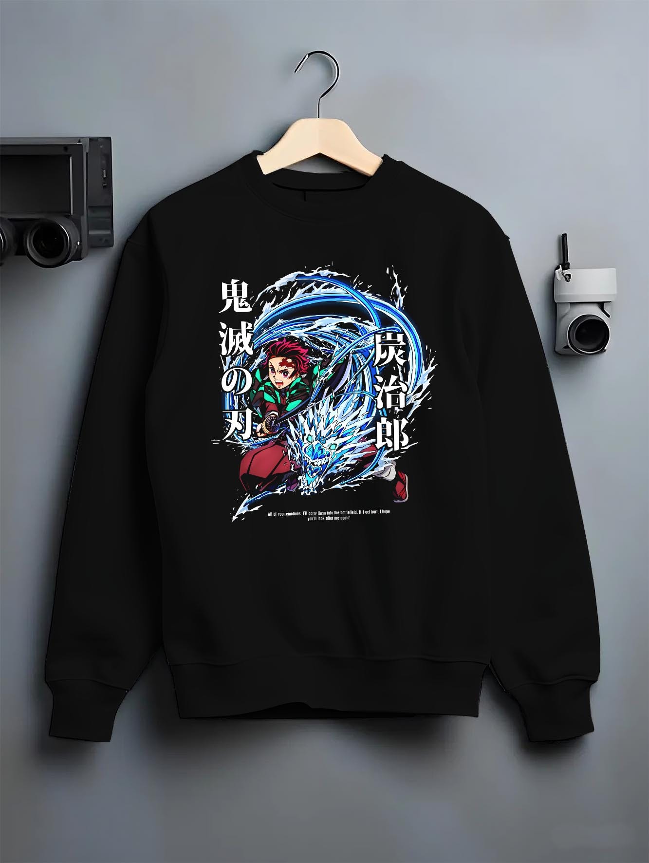 Black crewneck sweatshirt on a hanger against a grey wall, featuring Tanjiro Kamado Demon Slayer animation streetwear graphic with Water Breathing dragon and sword motion.