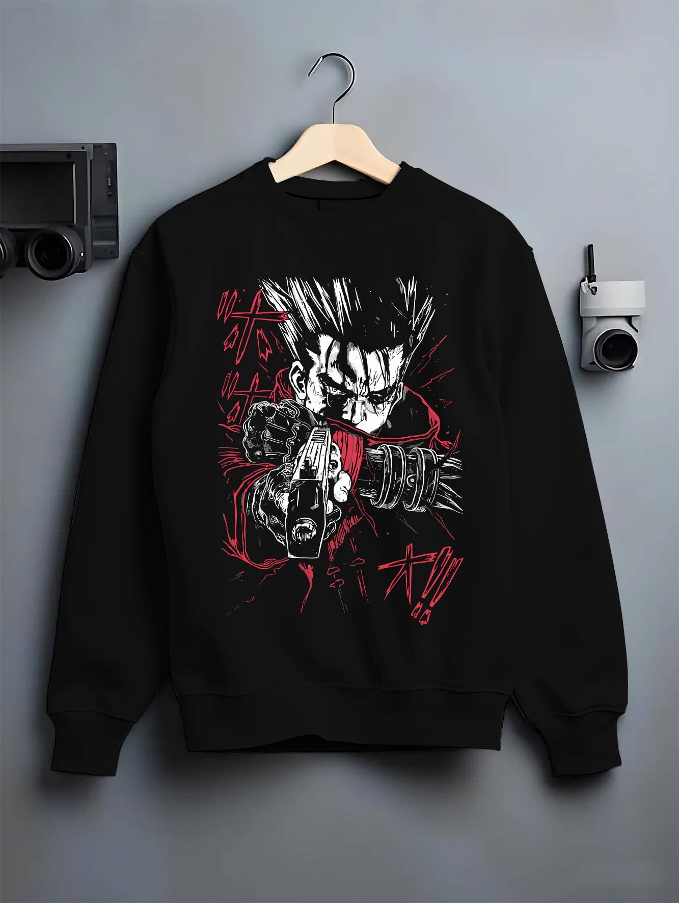 Black crewneck sweatshirt on a hanger against a grey wall, featuring Vash the Stampede dark manga panel design with retro anime-inspired weapon artwork.