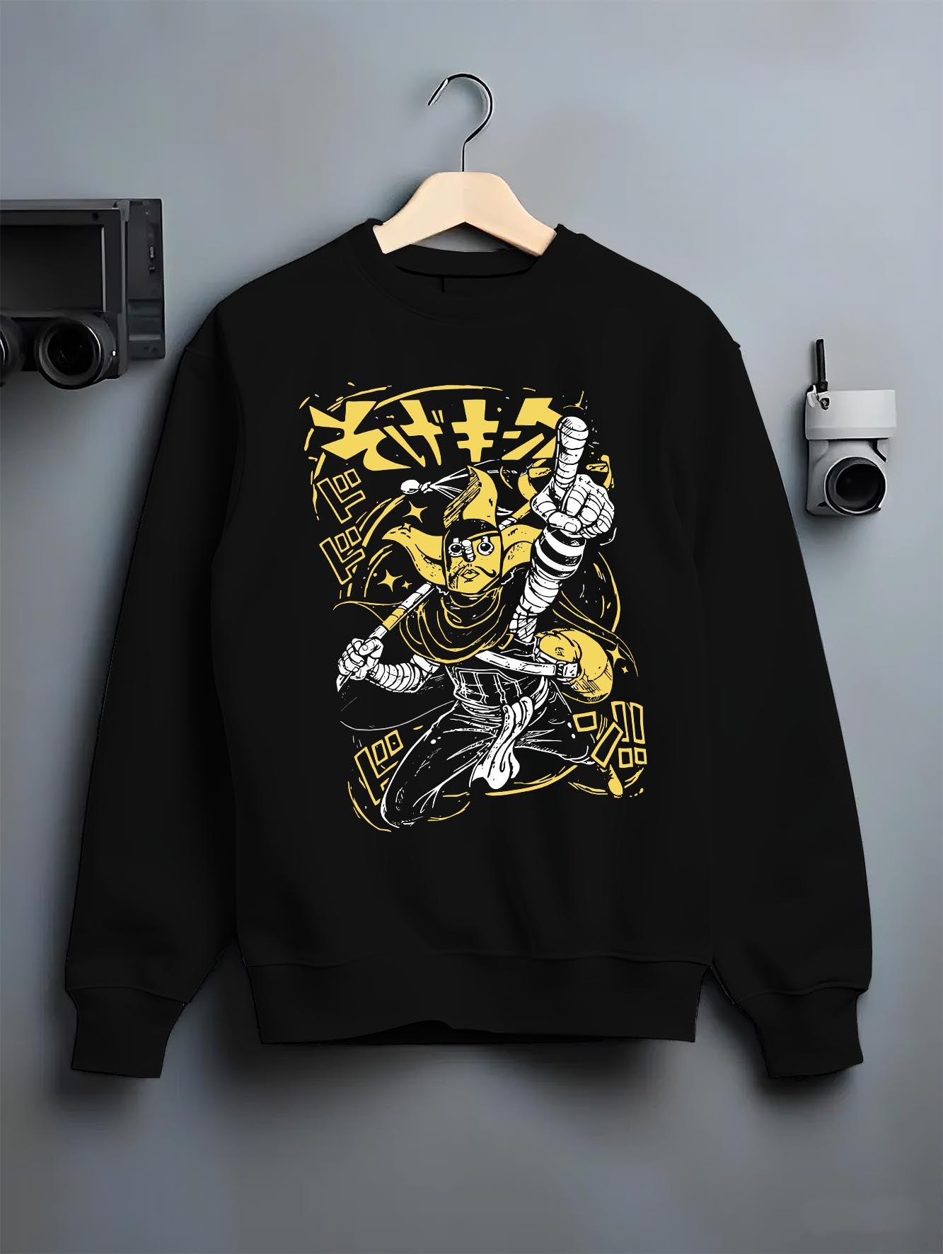 Black crewneck sweatshirt on a hanger against a grey wall, featuring JoJo’s Bizarre Adventure The World Stand anime poster inspired artwork in bold yellow retro style.