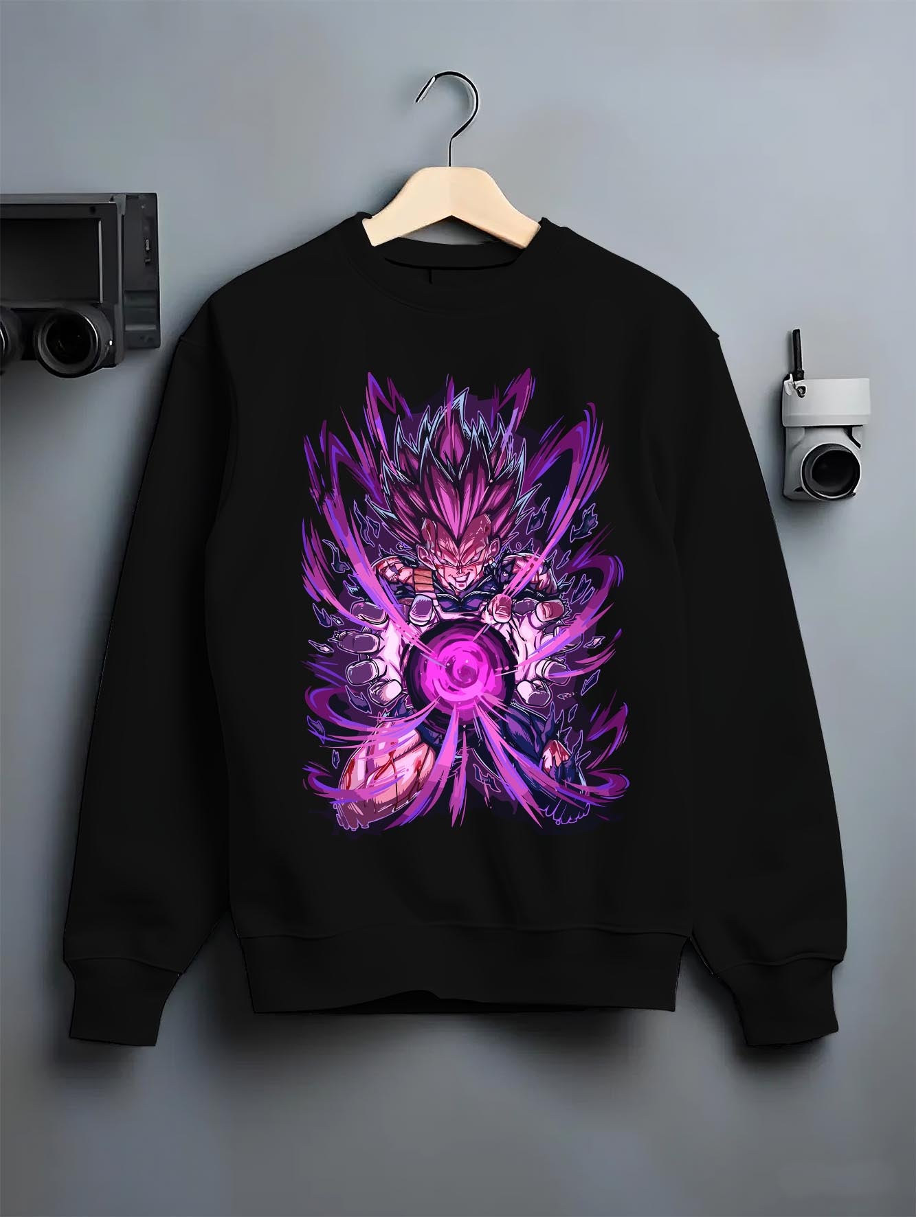 Black crewneck sweatshirt on a hanger against a grey wall, featuring Dragon Ball Vegeta anime poster inspired design with shonen battle aura and retro manga graphic.