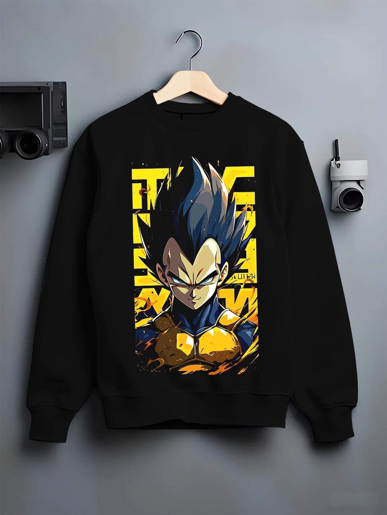 Black crewneck sweatshirt on a hanger against a grey wall, featuring Dragon Ball Vegeta anime poster inspired design with retro manga graphic style and yellow background.