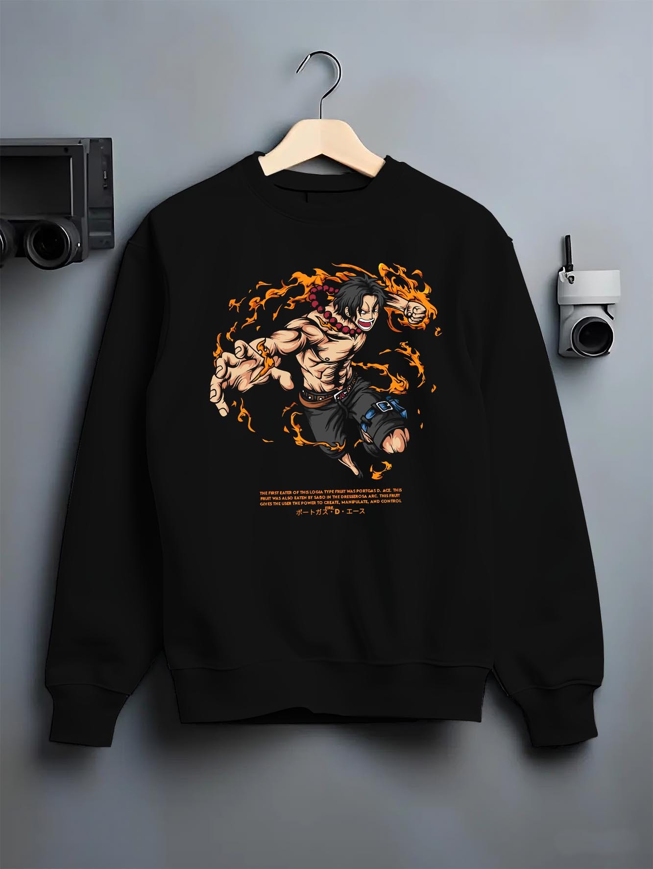 Black crewneck sweatshirt on a hanger against a grey wall, featuring Portgas D. Ace anime poster inspired design with fire powers from One Piece manga artwork print.