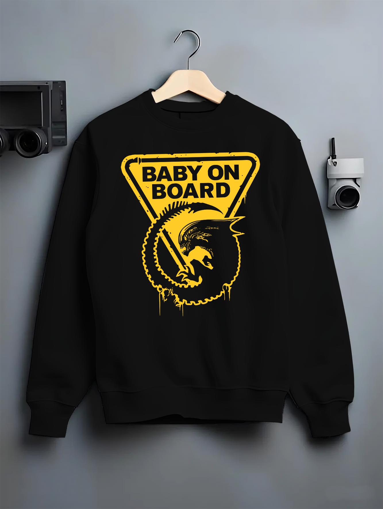 Black crewneck sweatshirt on hanger against grey wall, Alien baby on board retro sci-fi back graphic with triangle sign and drips.