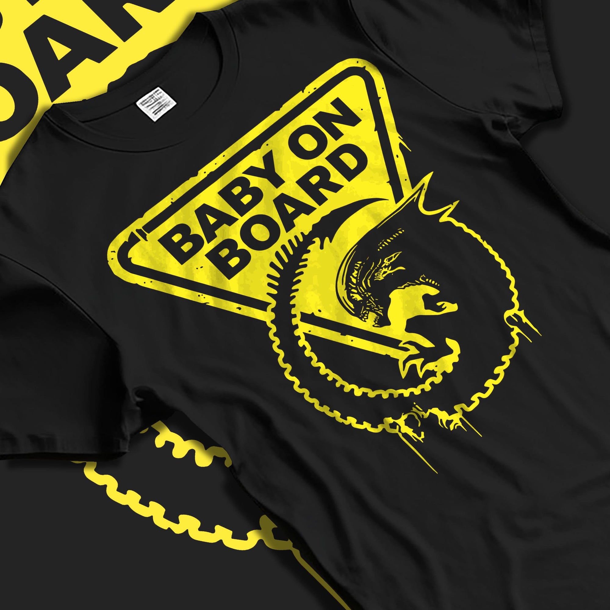 Black T-shirt laid flat with soft folds, featuring Alien baby on board warning sign design with distressed yellow drips.