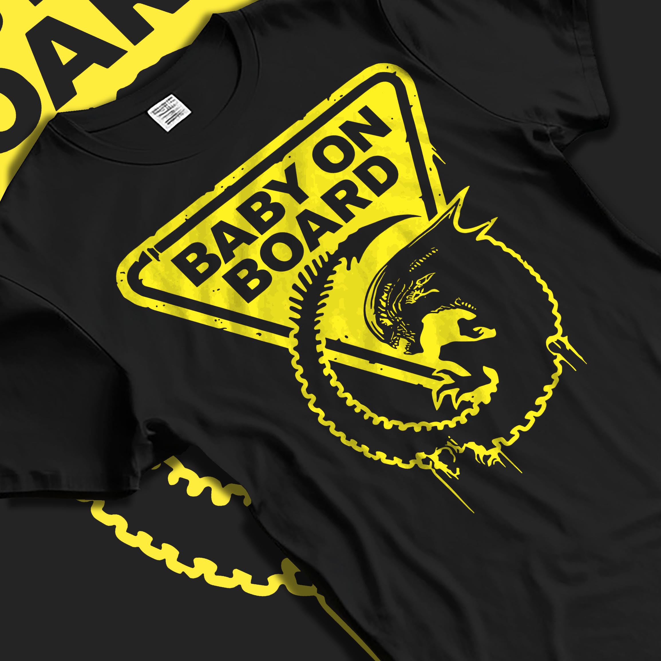 Black T-shirt laid flat with soft folds, featuring Alien baby on board warning sign design with distressed yellow drips.