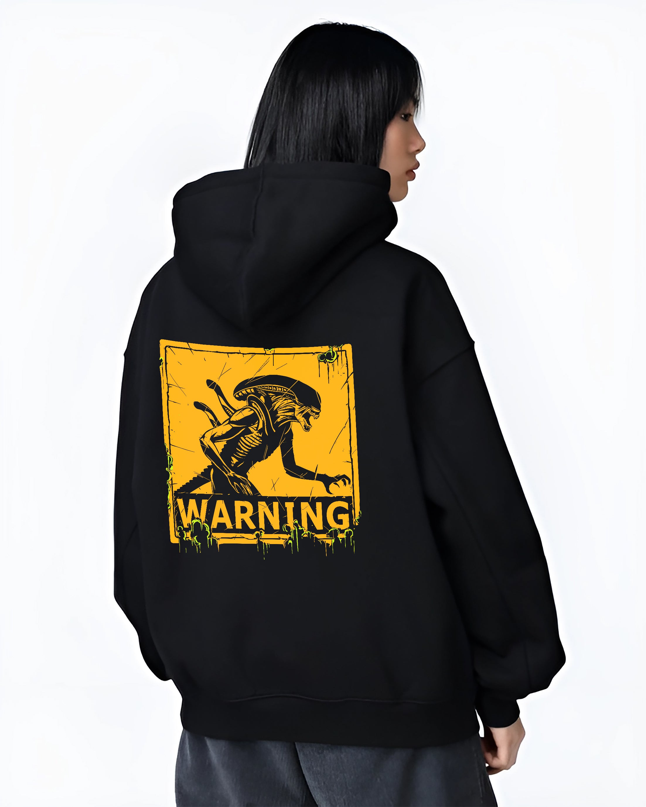 Black hoodie on female model, back view, Alien Xenomorph warning sign graphic with retro sci-fi vibe and green drips.