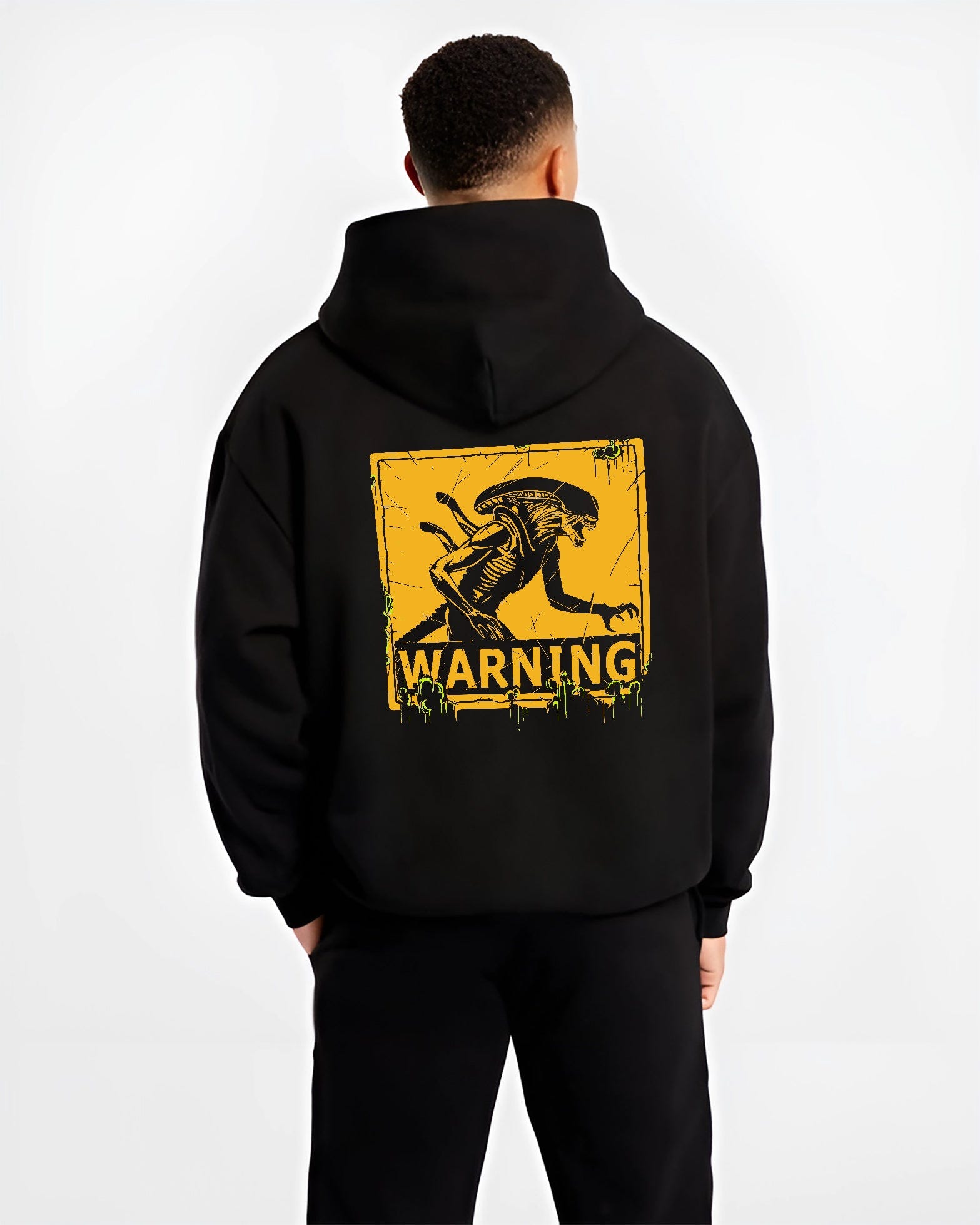Black hoodie on male model, back view, Alien Xenomorph warning sign design in retro sci-fi style with acid-green drips.