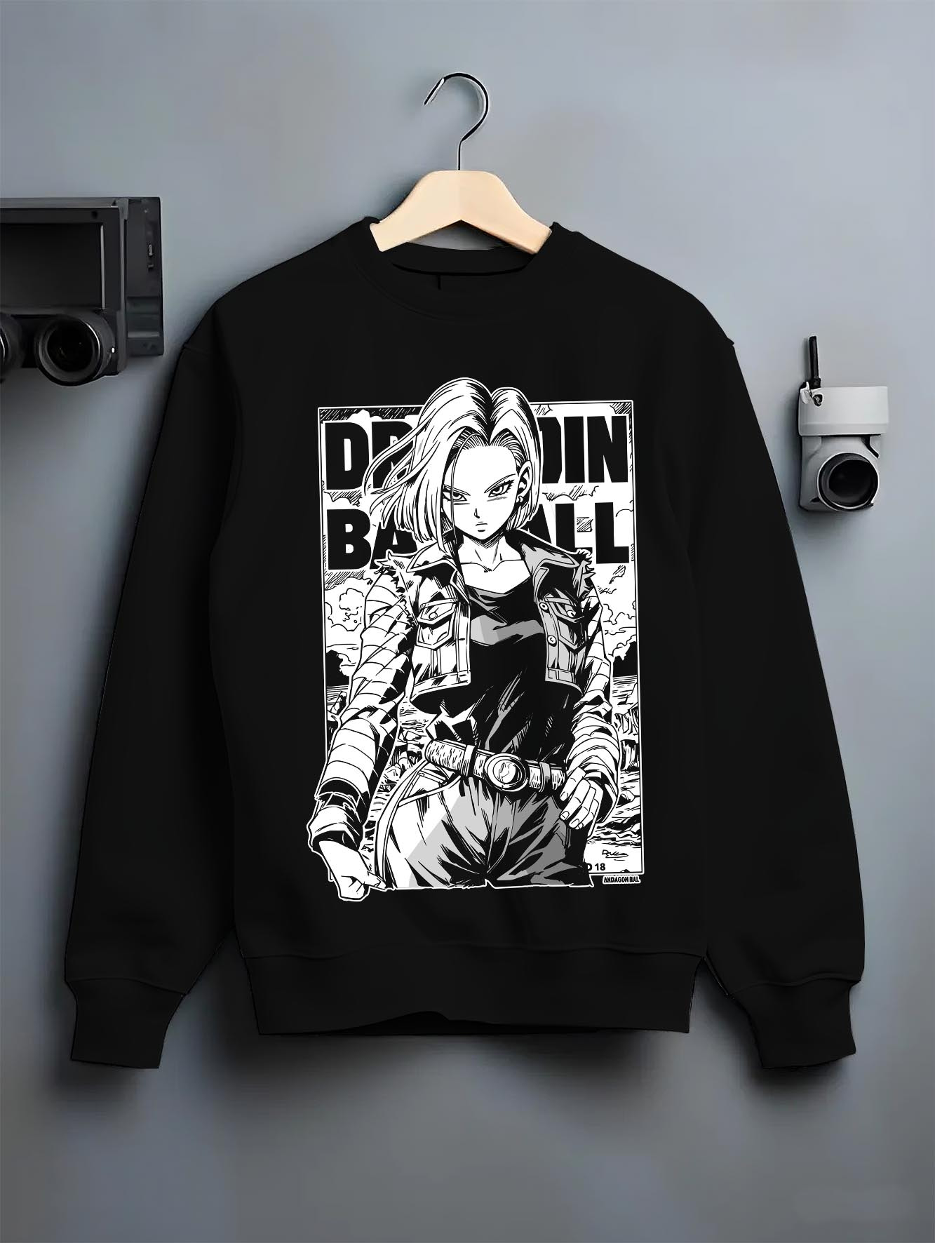 Black crewneck sweatshirt on a hanger against a grey wall, featuring Dragon Ball Android 18 dark manga panel artwork with bold retro anime streetwear graphic design.