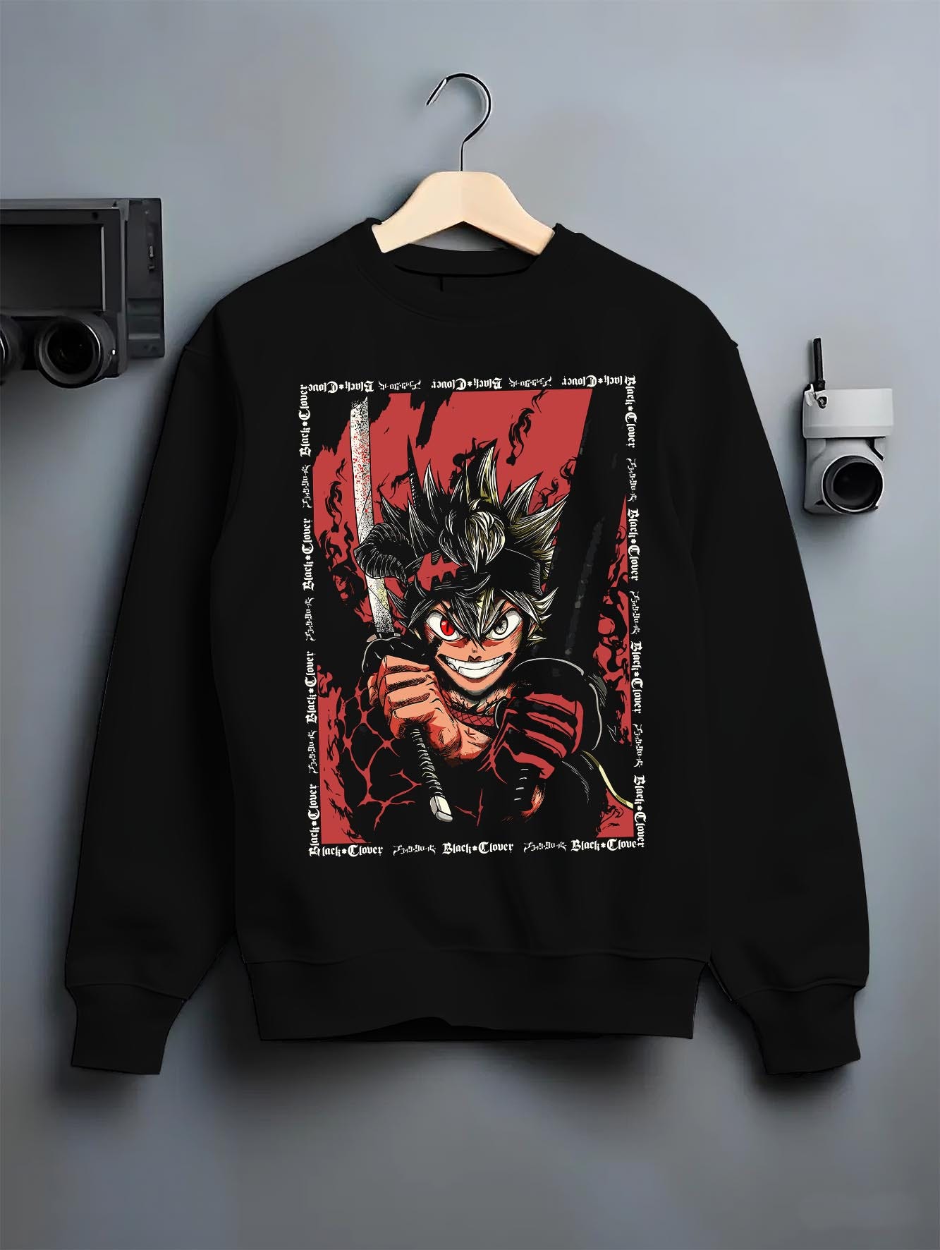 Black crewneck sweatshirt on a hanger against a grey wall, featuring Asta Black Clover anime poster inspired graphic with sword and intense red shonen battle aura.