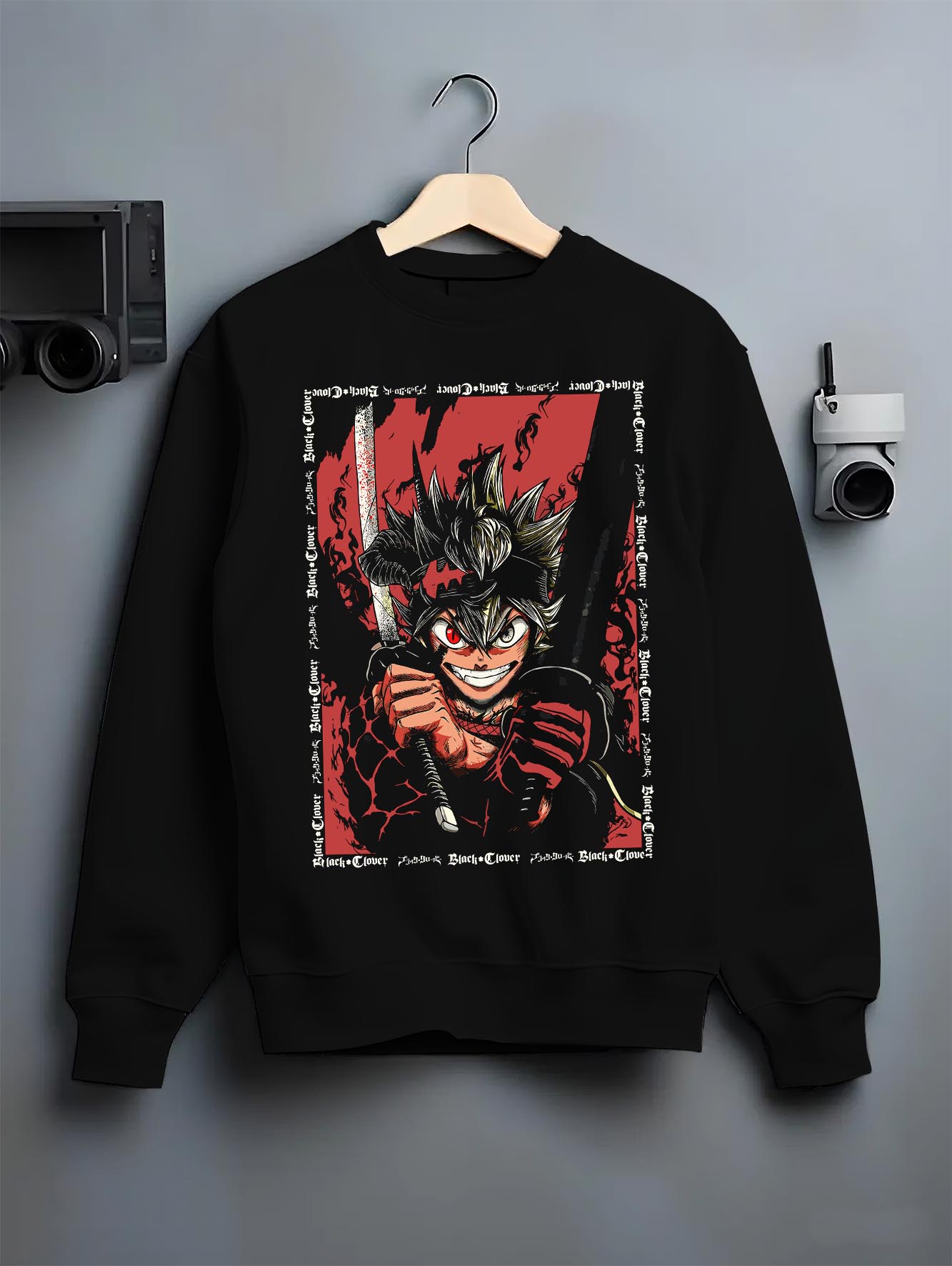 Black crewneck sweatshirt on a hanger against a grey wall, featuring Asta Black Clover anime poster inspired graphic with sword and intense red shonen battle aura.