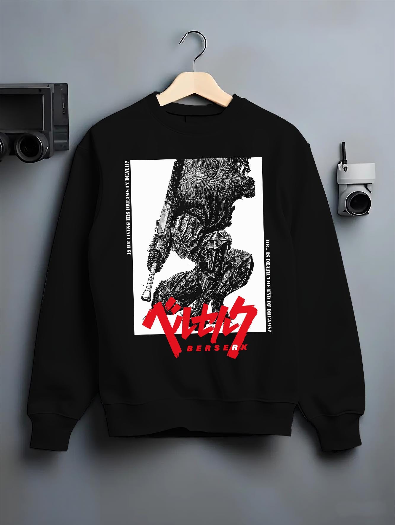 Black crewneck sweatshirt on a hanger against a grey wall, featuring Berserk Guts anime poster inspired design in dark manga panel style with sword stance artwork.