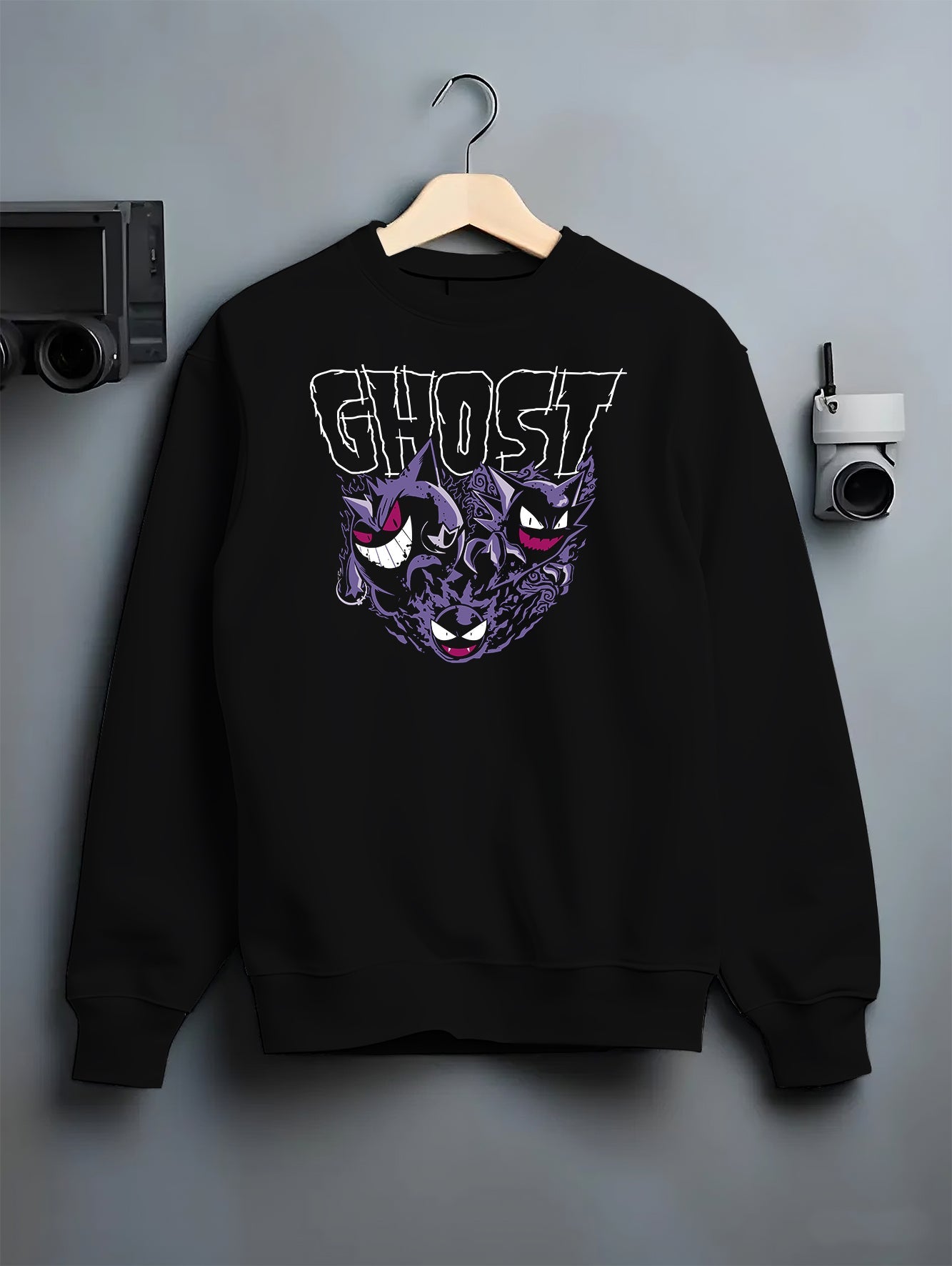 Black crewneck sweatshirt on hanger against grey wall, featuring Gengar, Haunter, Gastly retro game graphic with “GHOST” text and purple aura.