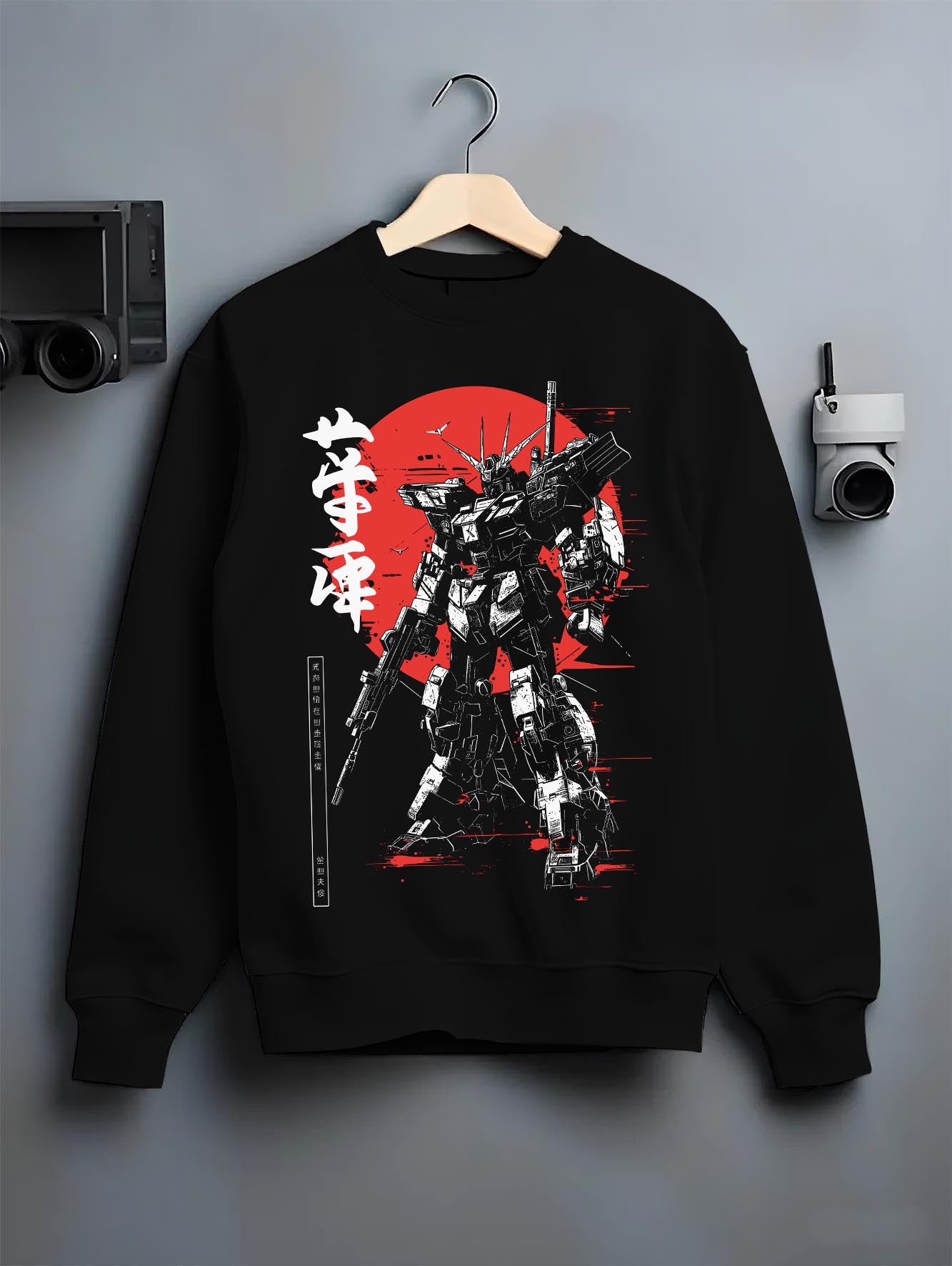 Black crewneck sweatshirt on a hanger against a grey wall, featuring Gundam retro mecha inspired graphic with bold Japanese sun backdrop in striking poster style.