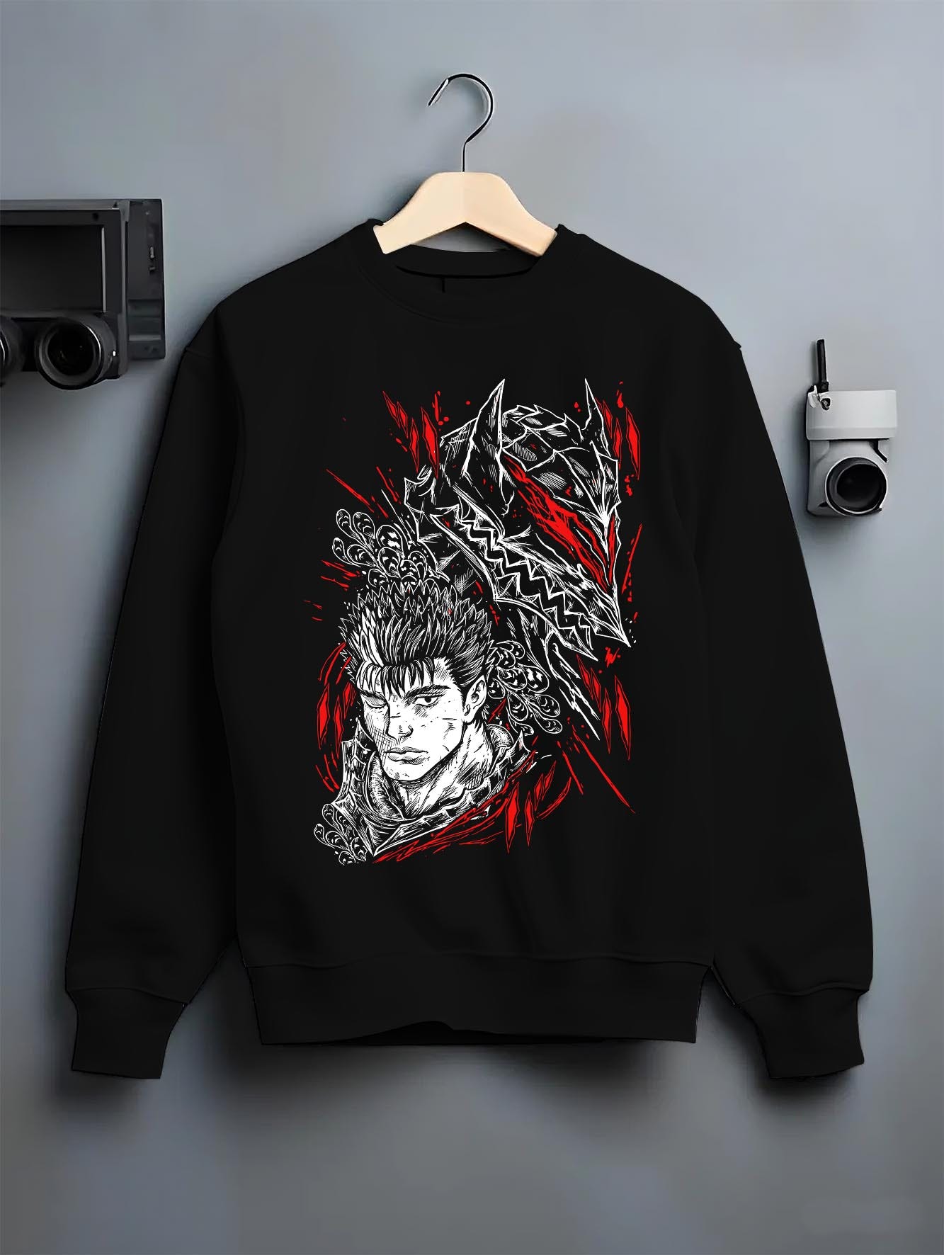 Black crewneck sweatshirt on a hanger against a grey wall, featuring Guts Berserk anime poster inspired design with manga panel graphic in striking red accents.