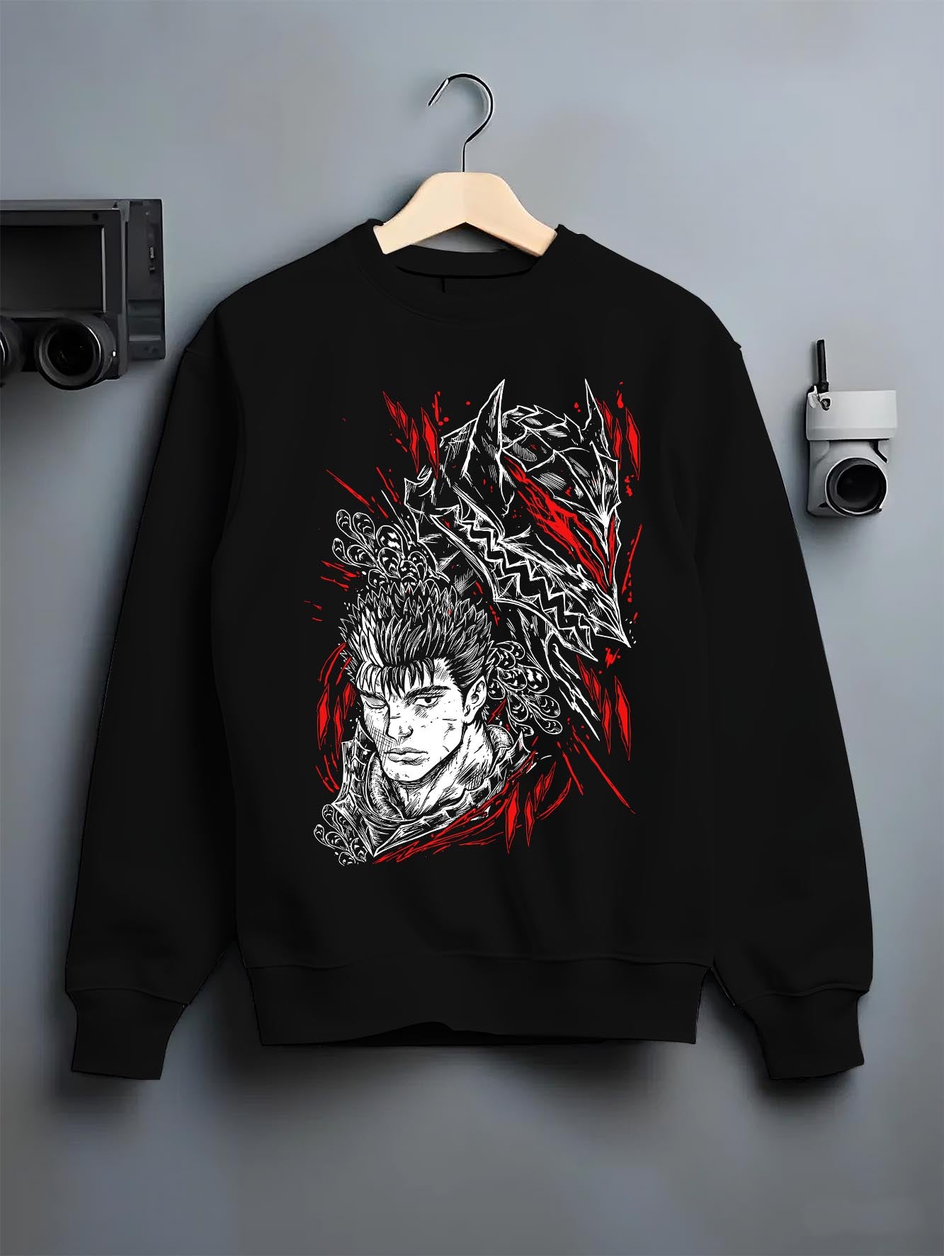 Black crewneck sweatshirt on a hanger against a grey wall, featuring Guts Berserk anime poster inspired design with manga panel graphic in striking red accents.