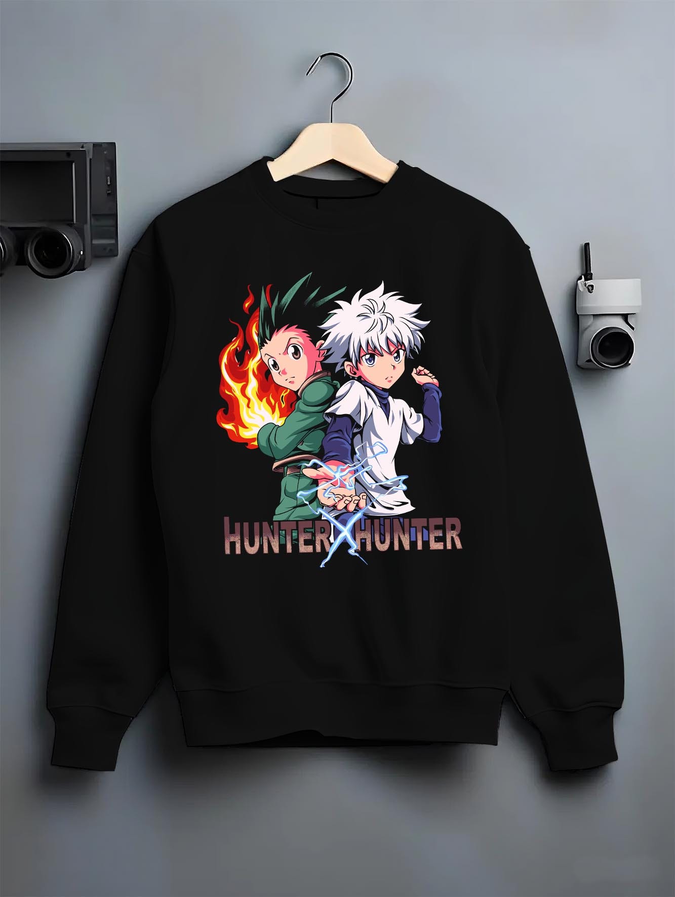 Black crewneck sweatshirt on hanger against grey wall, showing Hunter x Hunter Gon and Killua retro manga pixel graphic.