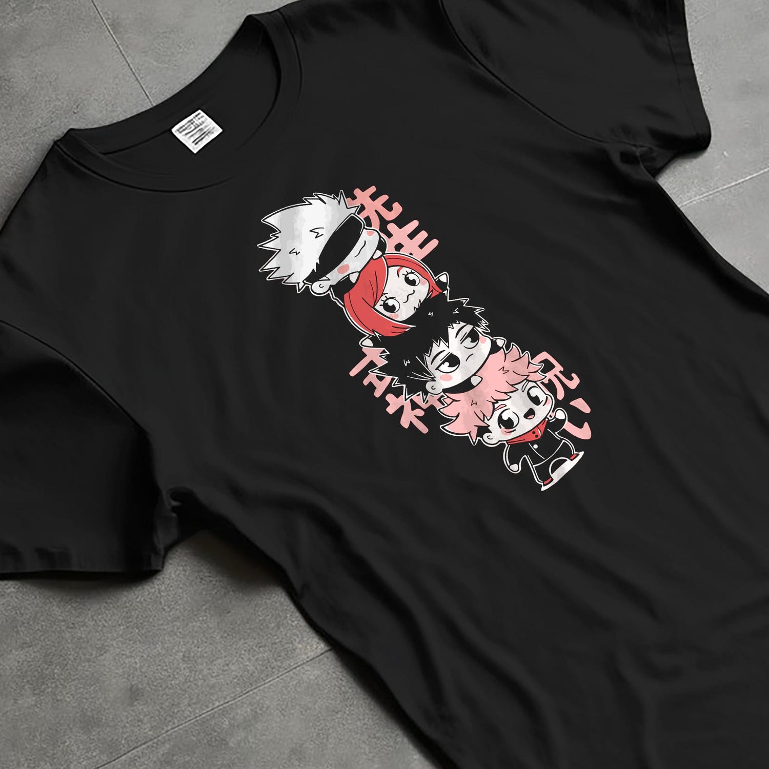 Black T-shirt laid flat with natural folds, featuring Jujutsu Kaisen chibi column graphic and soft pink Japanese lettering.