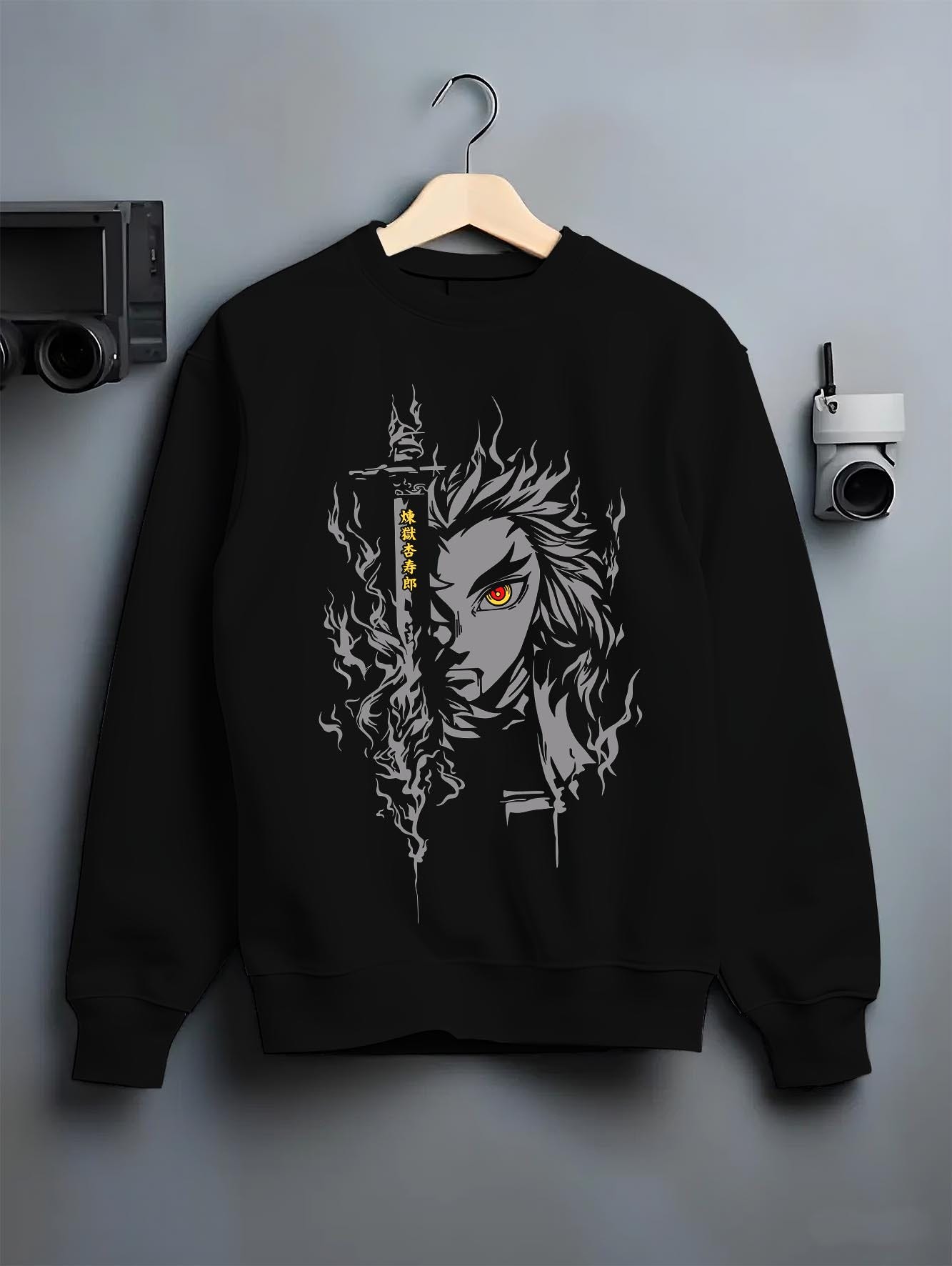 Black crewneck sweatshirt on a hanger against a grey wall, featuring Demon Slayer Rengoku anime poster inspired artwork with fiery aura in dark retro manga panel style.