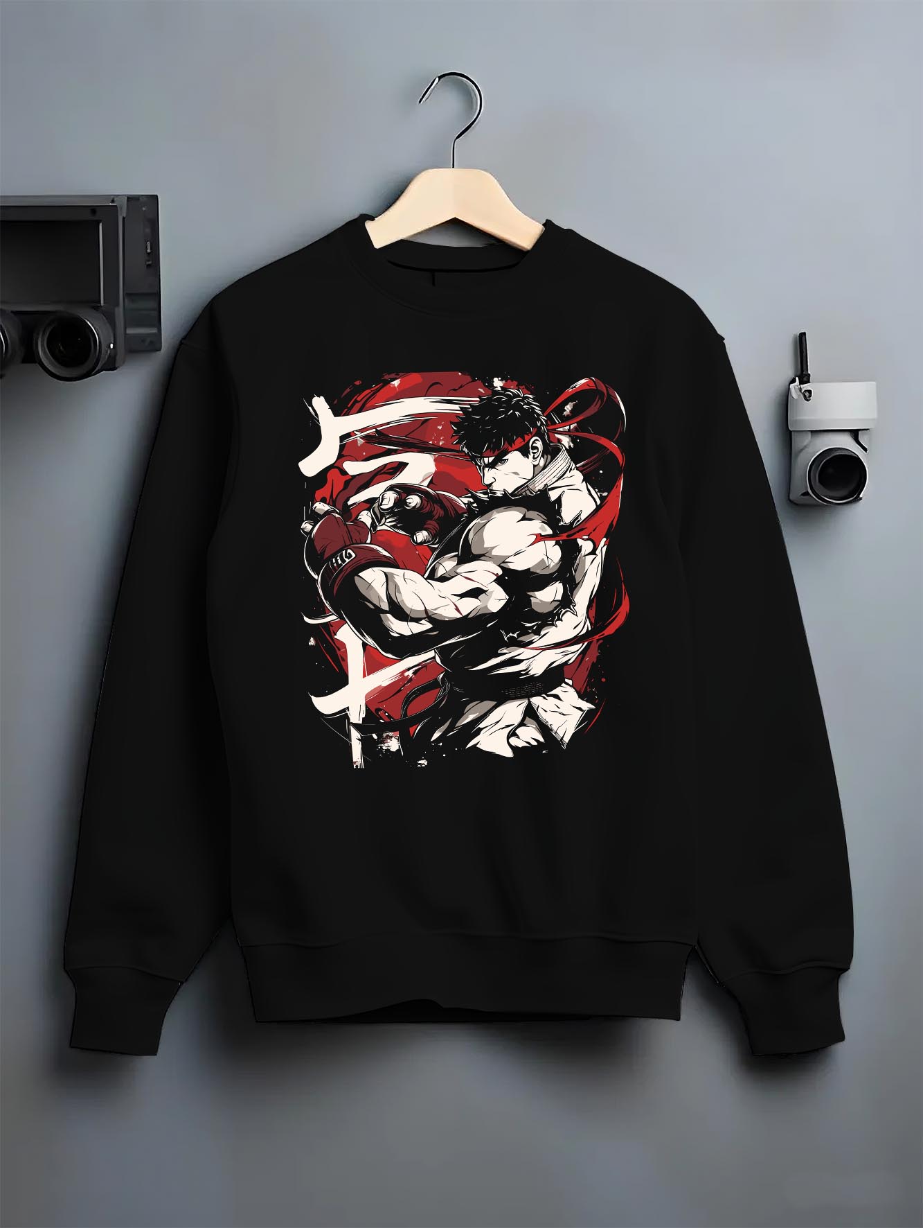 Black crewneck sweatshirt on a hanger against a grey wall, featuring Ryu Street Fighter retro streetwear graphic with iconic fighter pose and vivid red accen