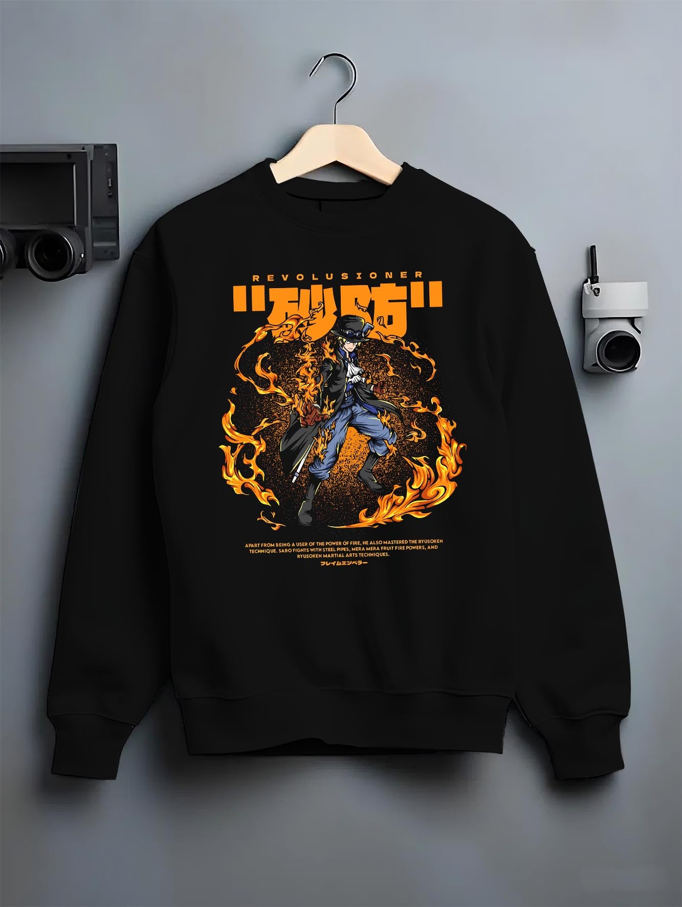 Black crewneck sweatshirt on a hanger against a grey wall, featuring Sabo One Piece fiery retro manga anime poster inspired graphic design