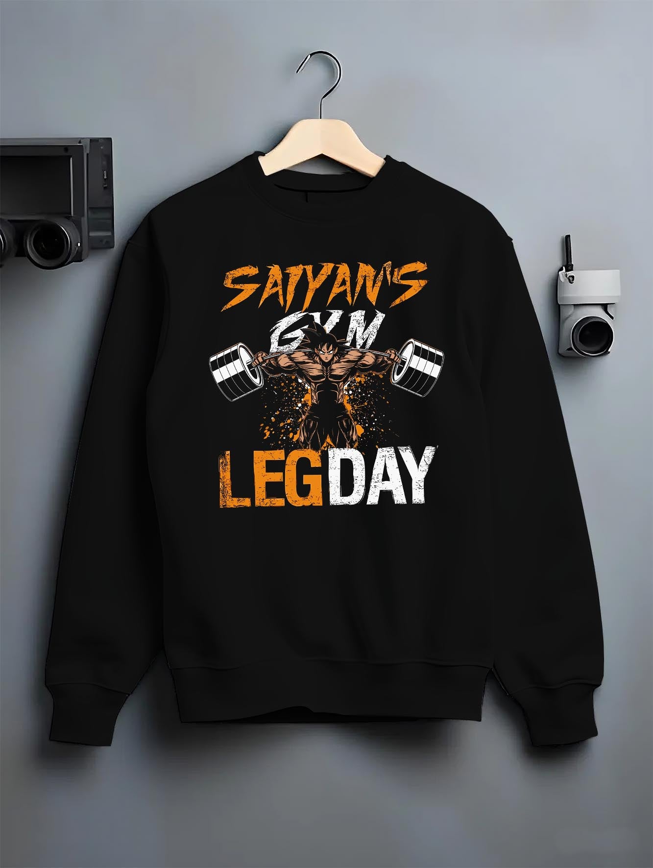 Black crewneck sweatshirt on a hanger against a grey wall, featuring Saiyan’s Gym Leg Day urban streetwear anime graphic with intense weightlifting shonen character design.