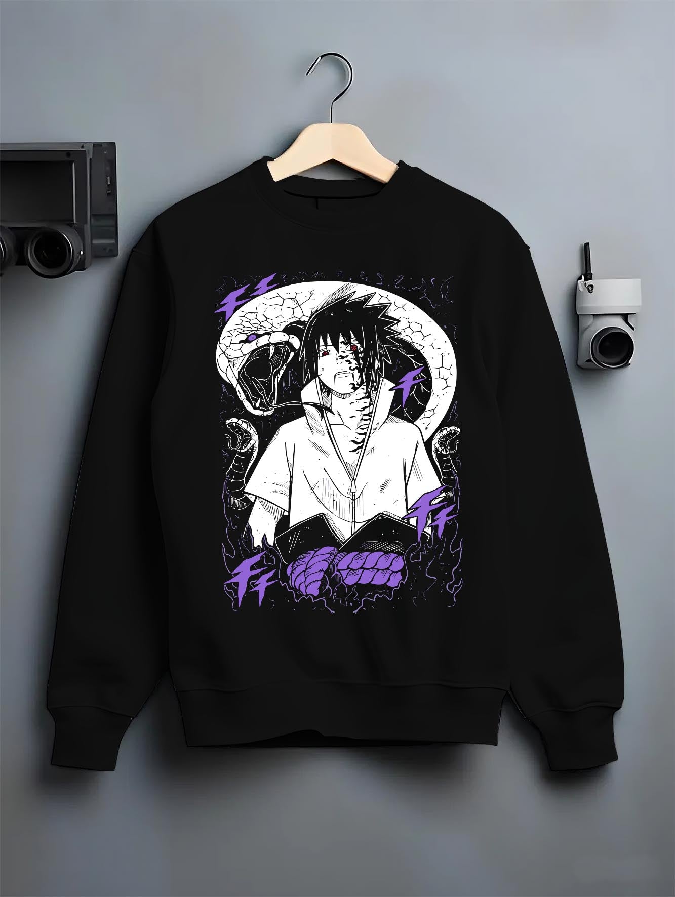 Black crewneck sweatshirt on a hanger against a grey wall, featuring Sasuke Naruto retro manga inspired artwork with serpent detail and Japanese streetwear aesthetic.