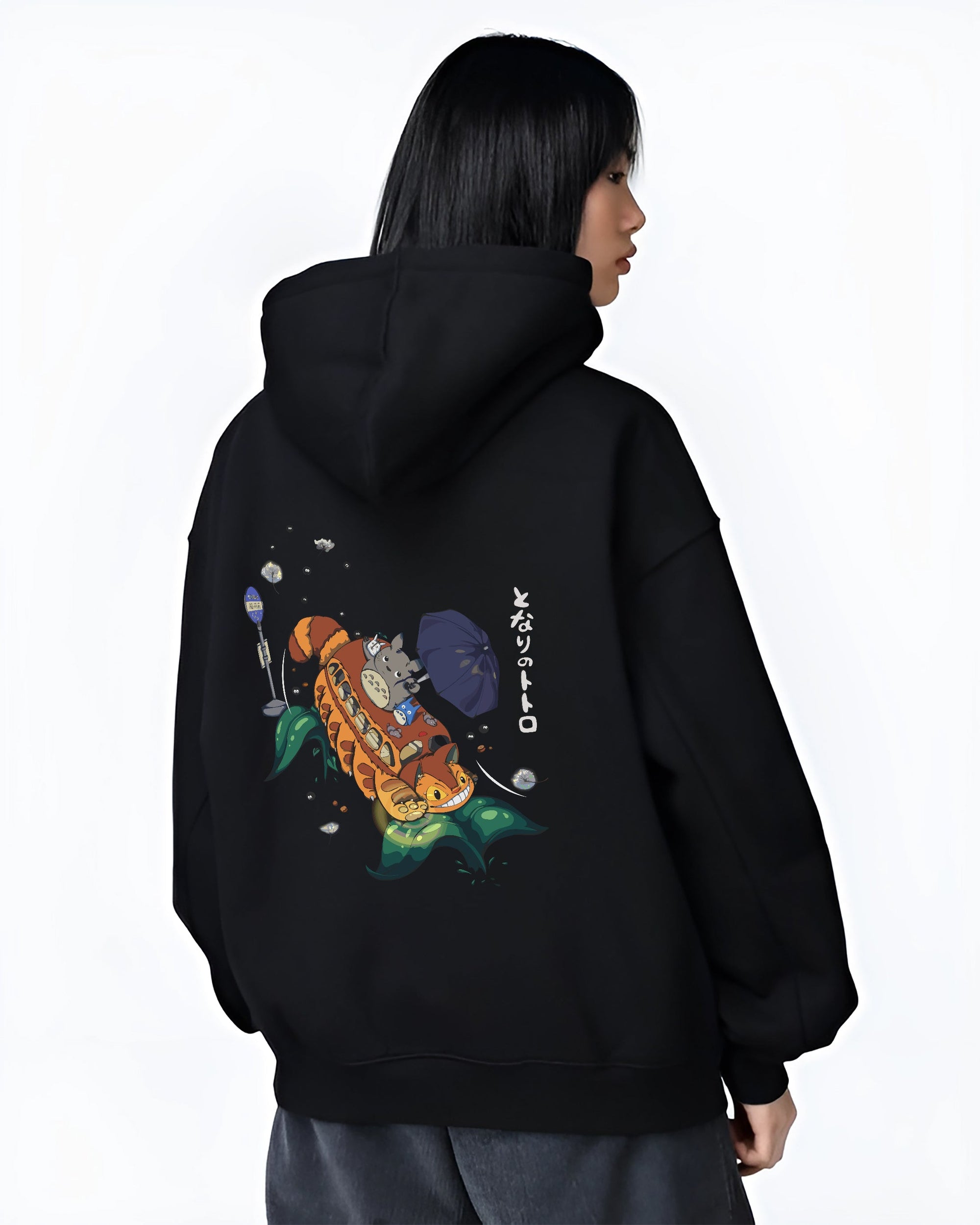 Black hoodie on female model, back view, Totoro with Catbus retro manga artwork, umbrella detail and floating soot sprites.