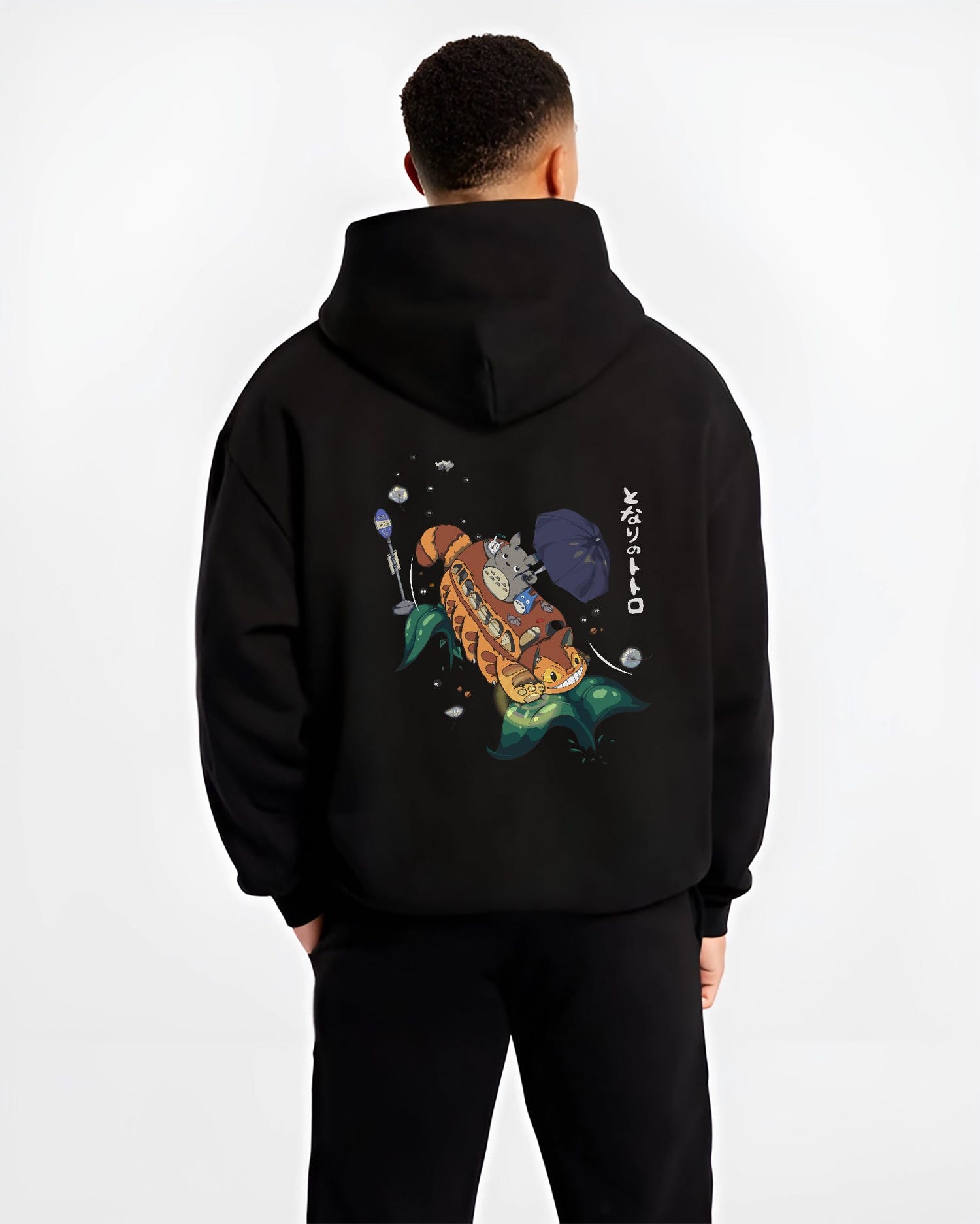 Black hoodie on male model, back view, Totoro and Catbus anime poster design with umbrella and soot sprites over stylized leaves.
