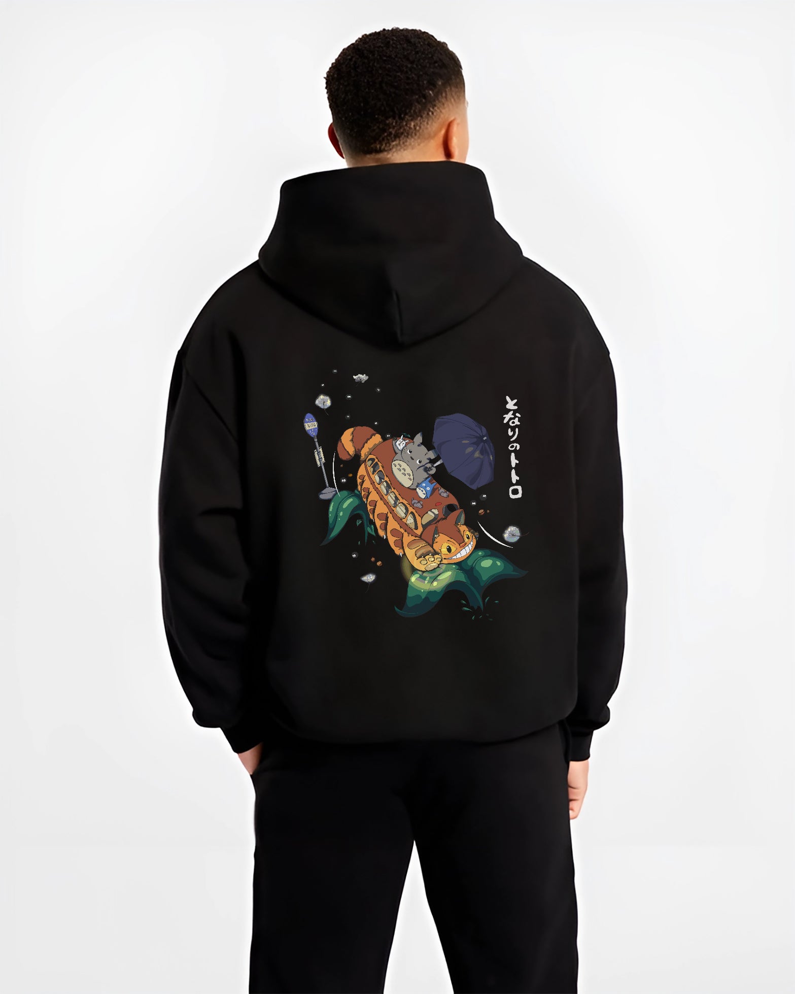 Black hoodie on male model, back view, Totoro and Catbus anime poster design with umbrella and soot sprites over stylized leaves.