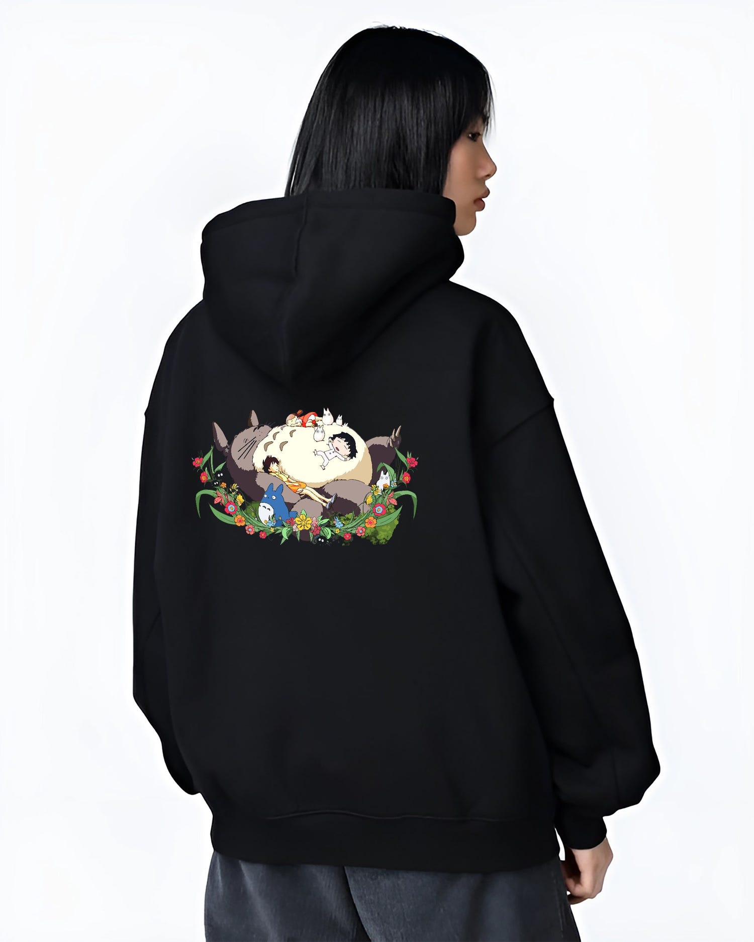 Black hoodie worn by a female model, back view, featuring Totoro nap artwork with forest flowers, Japanese animation streetwear, vintage retro aesthetic.